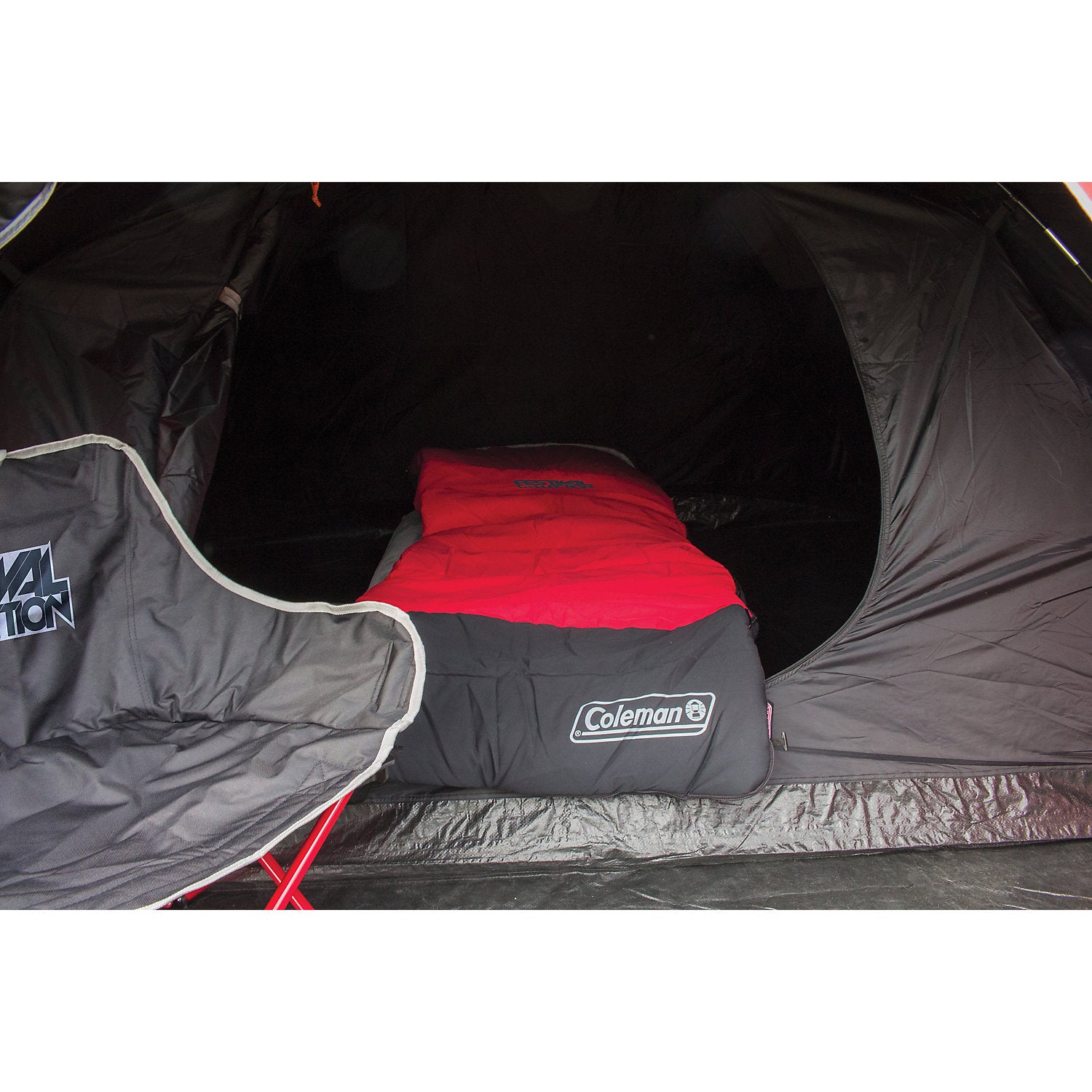 Roter und schwarzer Schlafsack der Festival Collection Single liegt im offenen Zelt auf einer roten Campingliege, Coleman-Logo sichtbar