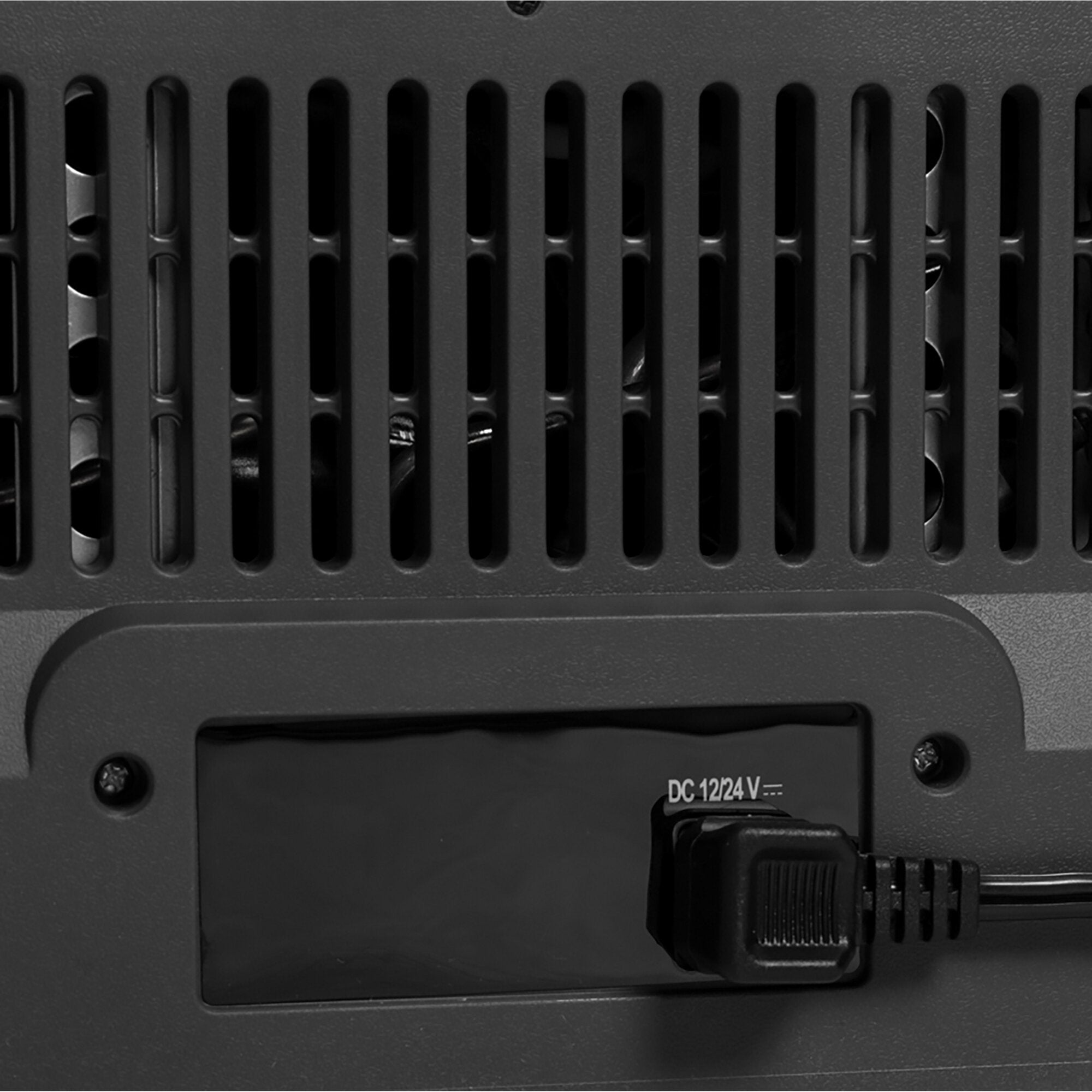 Rückseite einer dunklen Kühlbox mit vertikalen Lüftungsschlitzen und einem DC-12/24V-Anschluss, Schrauben sichtbar