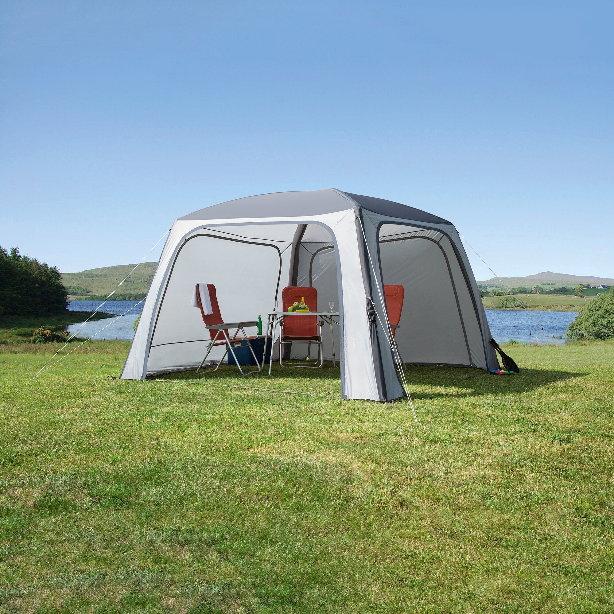 Pavillon Relax Air in hellgrau mit offener Front, rote Stühle und Tisch mit Obst und Getränken auf grünem Rasen unter blauem Himmel