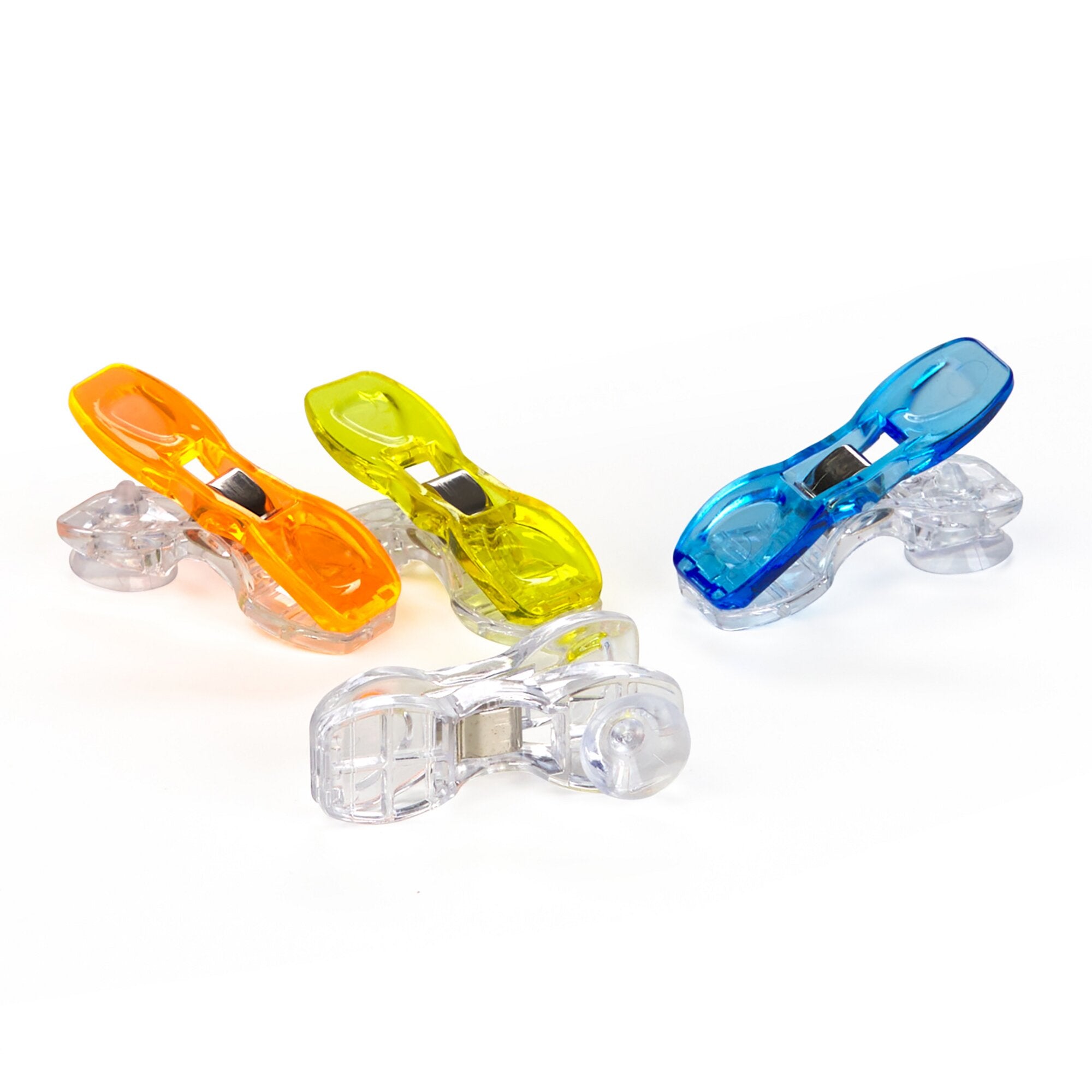 Mehrfarbige transparente Spannclips mit Saugnäpfen in Orange, Gelb und Blau liegen auf weißem Hintergrund