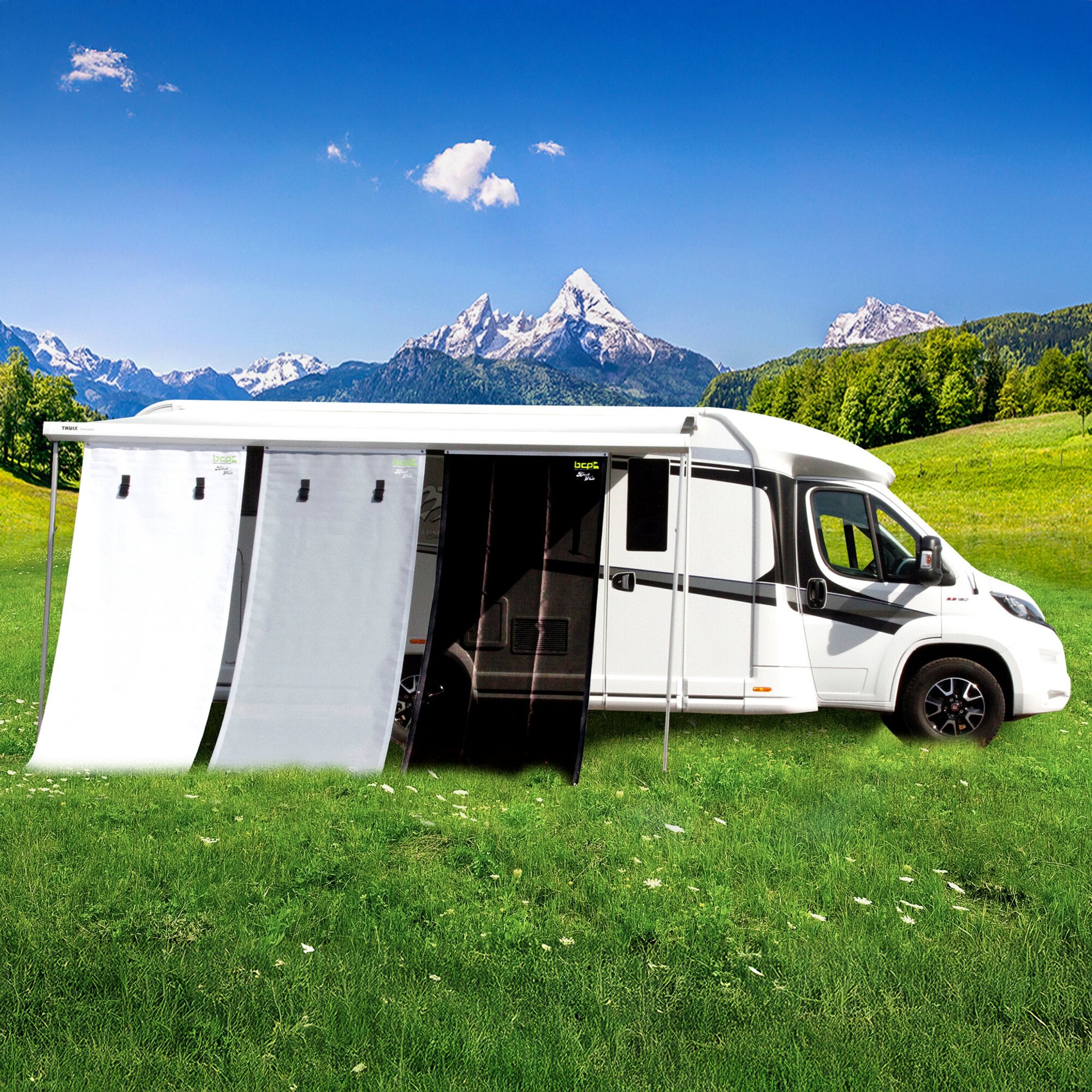 Weißes Wohnmobil mit grau-weißer ausziehbarer Seitenmarkise, Sichtschutz-Paneele hängen herab, grüne Wiese und Berglandschaft im Hintergrund