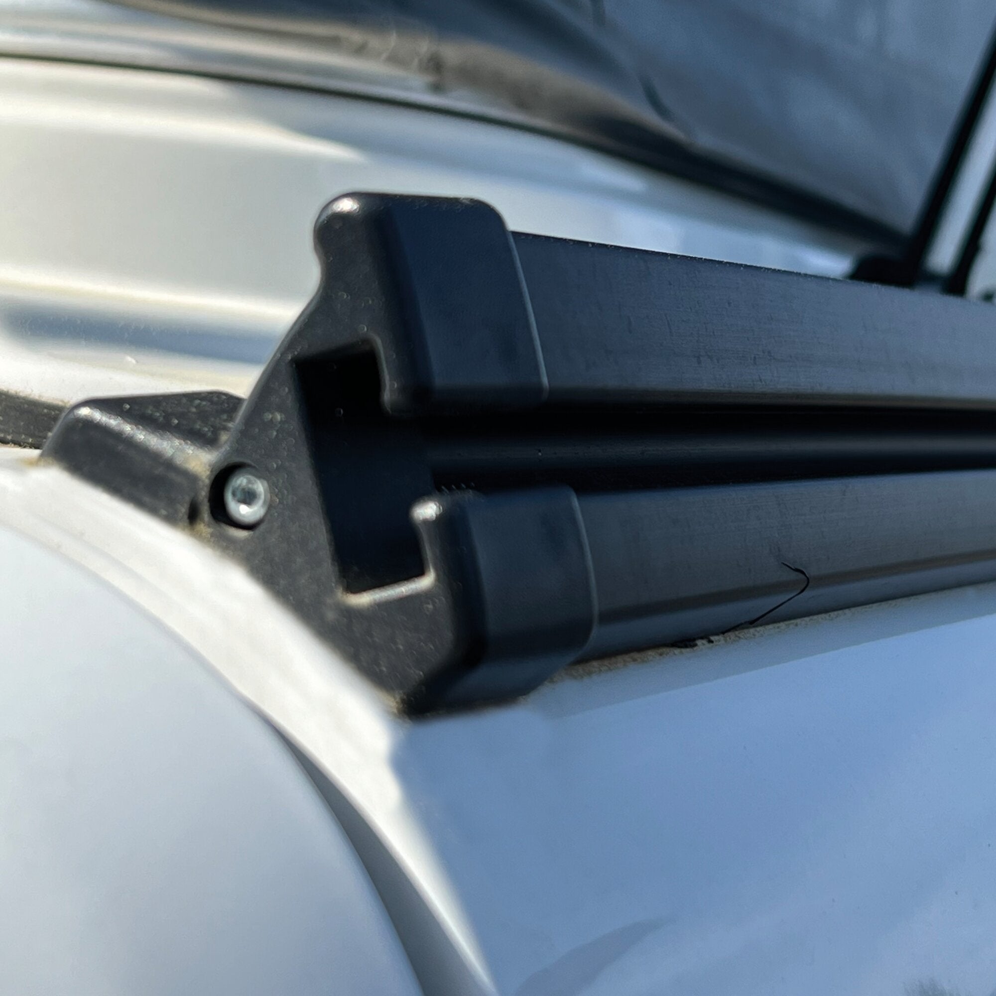 Schwarzer Adapter-Halter aus Kunststoff mit Schraube, befestigt an einer schwarzen Führung vor einer silbernen Metalloberfläche, Nahaufnahme