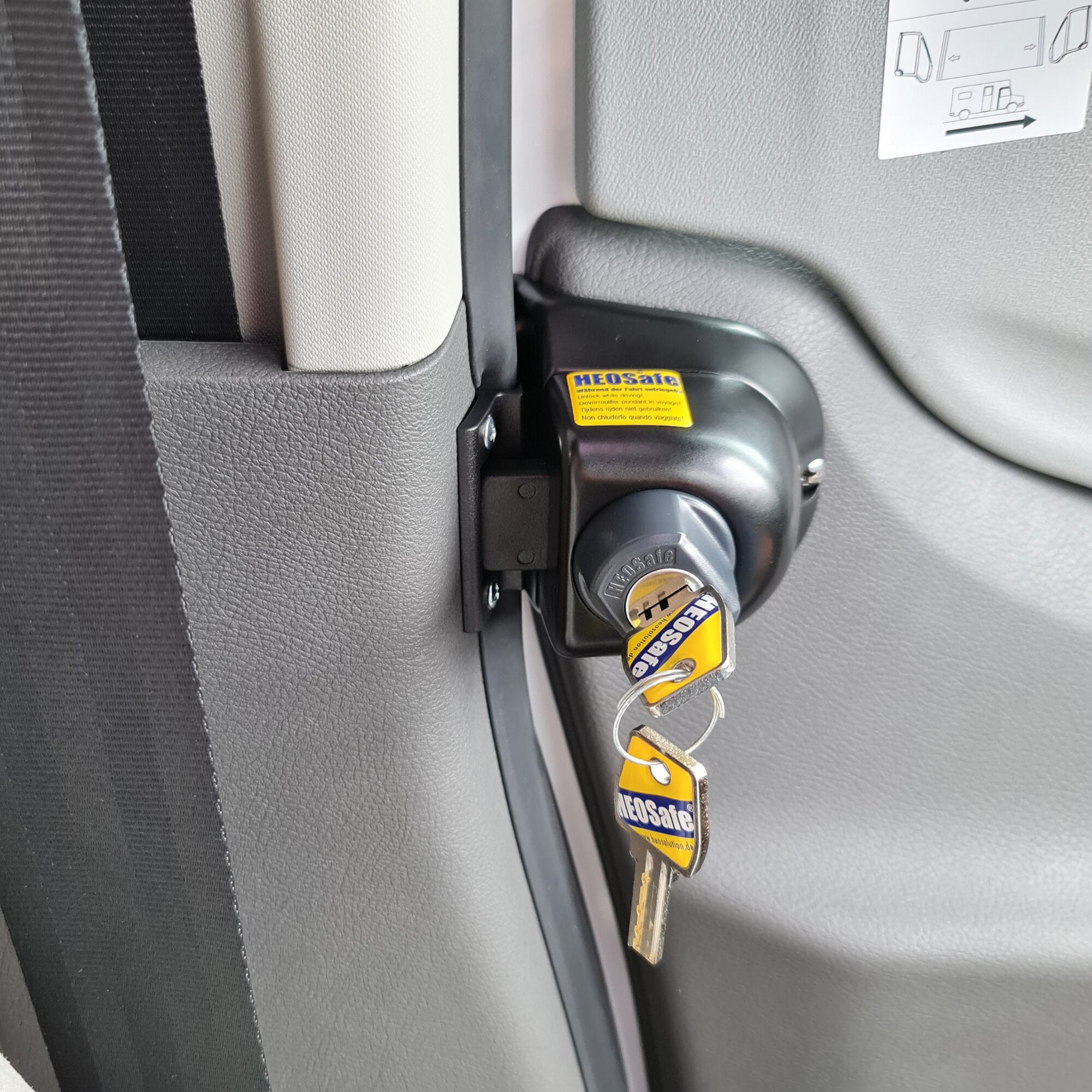 Innenraum am Türbereich des Fahrzeugs mit schwarzem Diebstahlschutzschloss am Türgriff, gelbem Warnaufkleber und Schlüssel mit HEOSafe-Tags