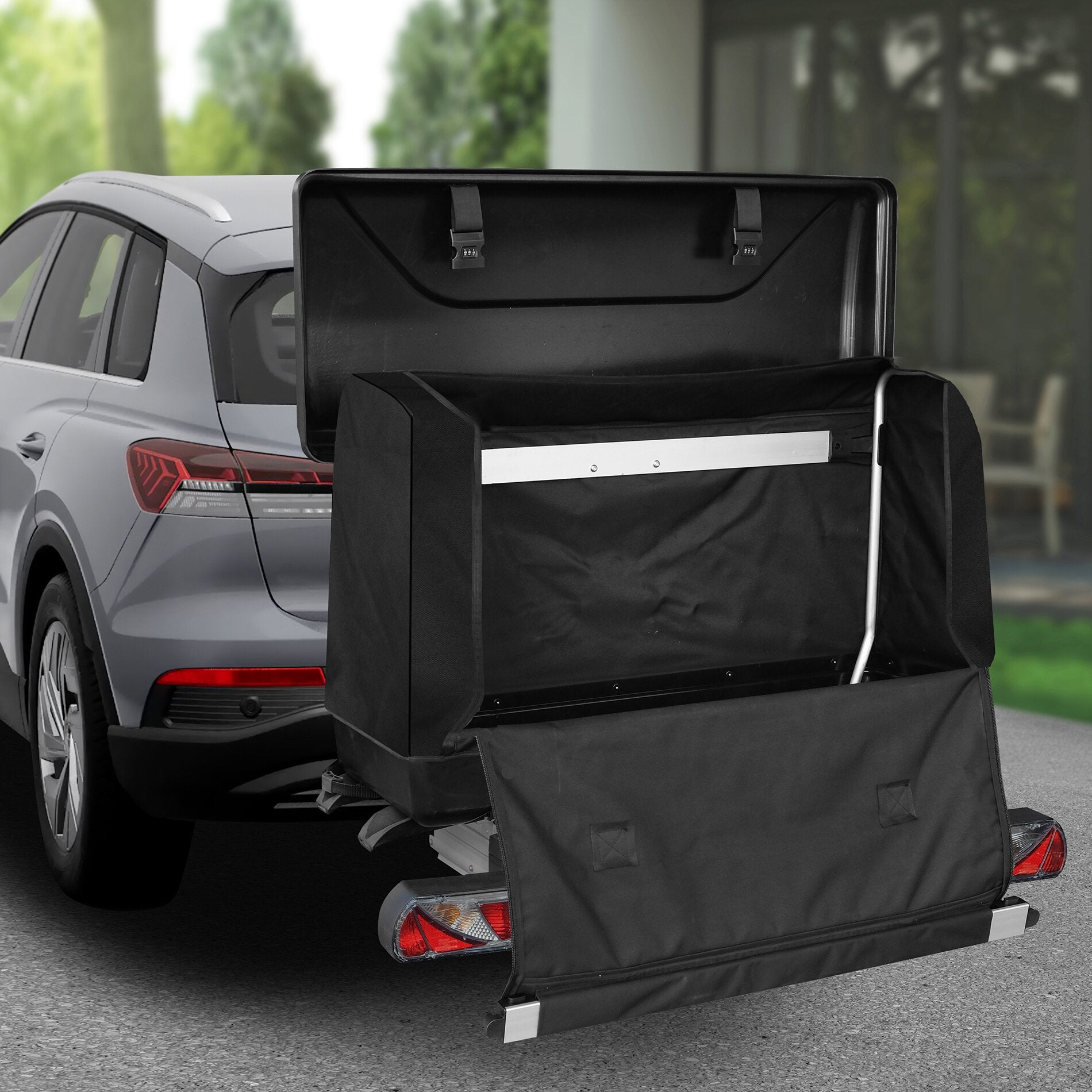 Schwarze Transportbox aus Stoff mit Metallrahmen, am Heck eines silbernen SUVs montiert; zwei Verschlussriemen mit Zahlenschloss sichtbar