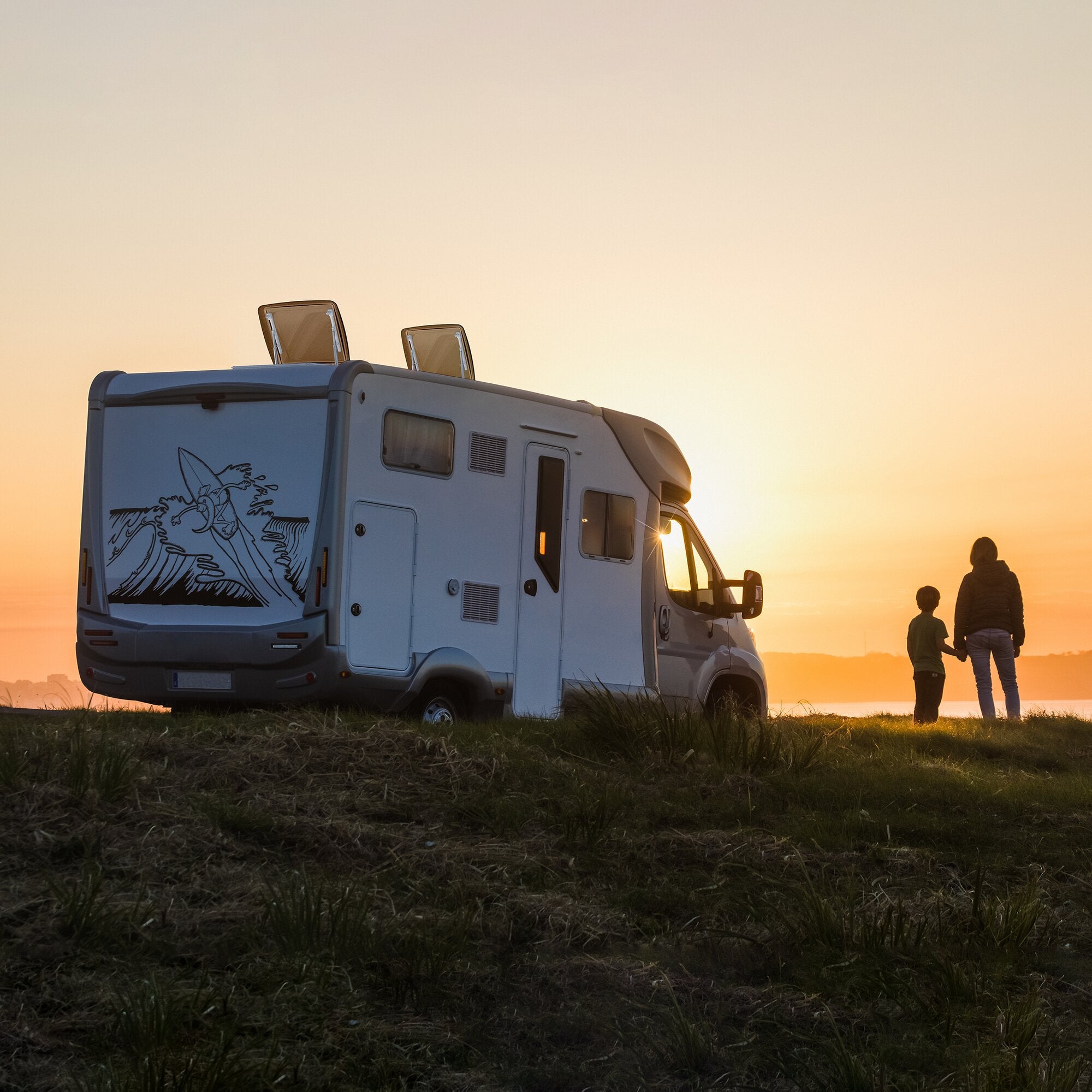 Seitlicher Blick auf ein weißes Wohnmobil bei Sonnenuntergang, zwei aufgeklappte Dachhauben auf dem Dach hinter der Fahrerkabine