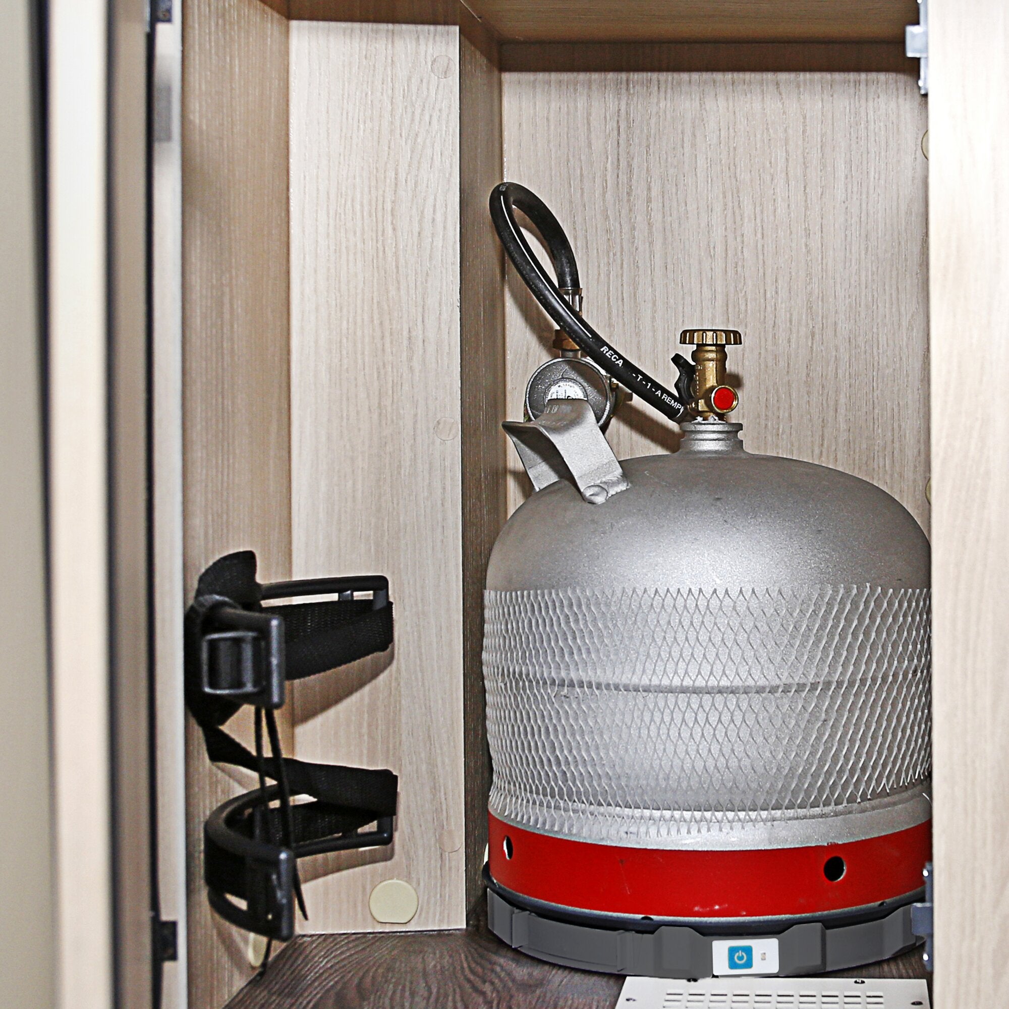 Innenansicht eines Schranks mit einer grauen Gasflasche, Regler, schwarzen Schläuchen und Holzverkleidung