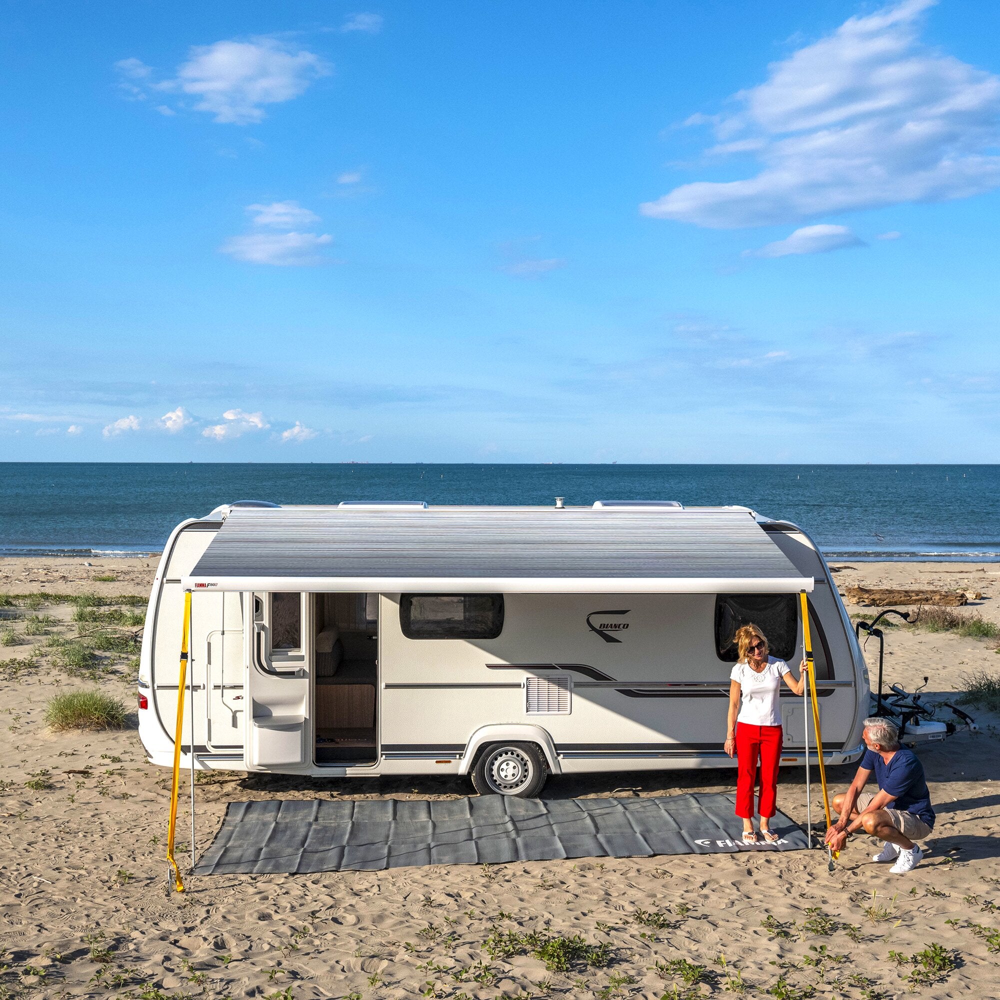 Caravan am Strand mit Markise F80 in Royal Grey, 290 cm, grauer Bodenbelag aus Matte, zwei Personen am Eingang
