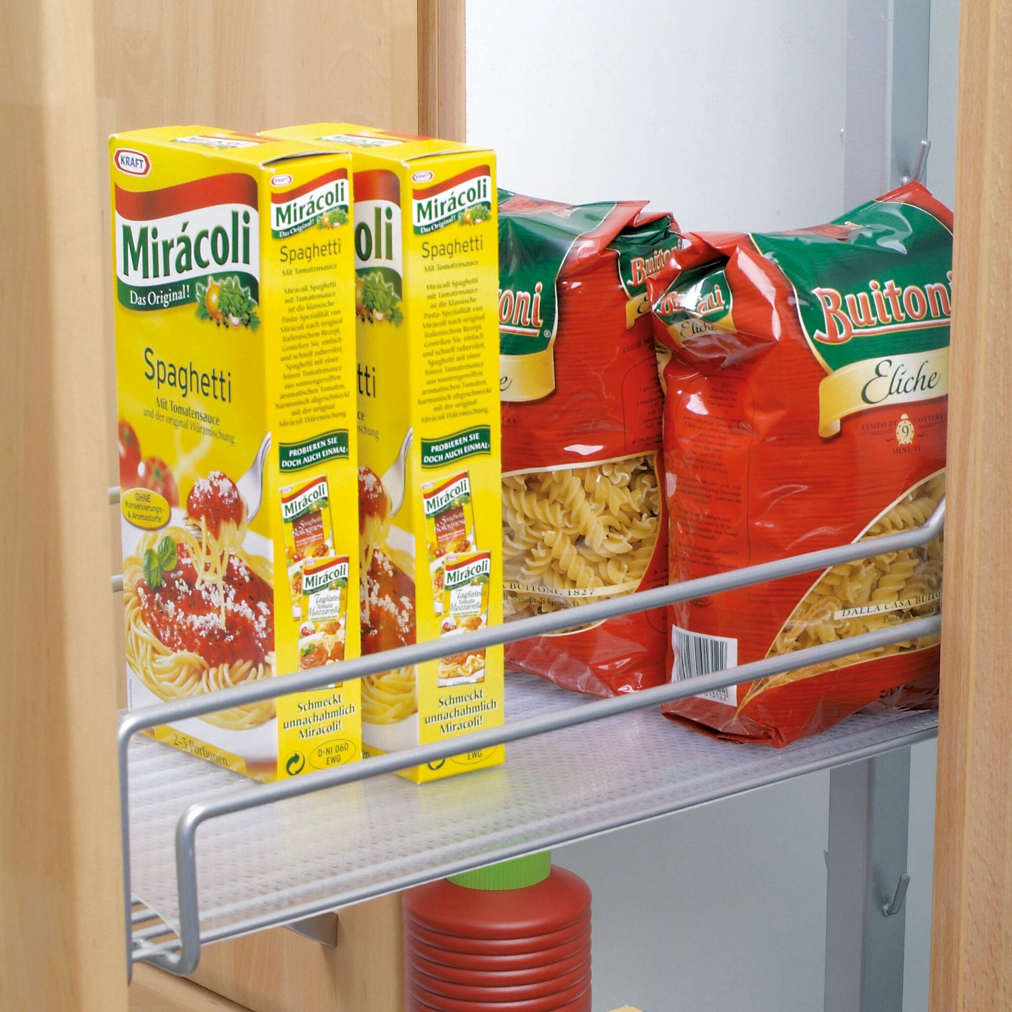 Gelbe Miracoli Spaghetti Kartons stehen links im Holzregal, daneben rote Buitoni Pasta-Beutel; sichtbare Metallregalstäbe