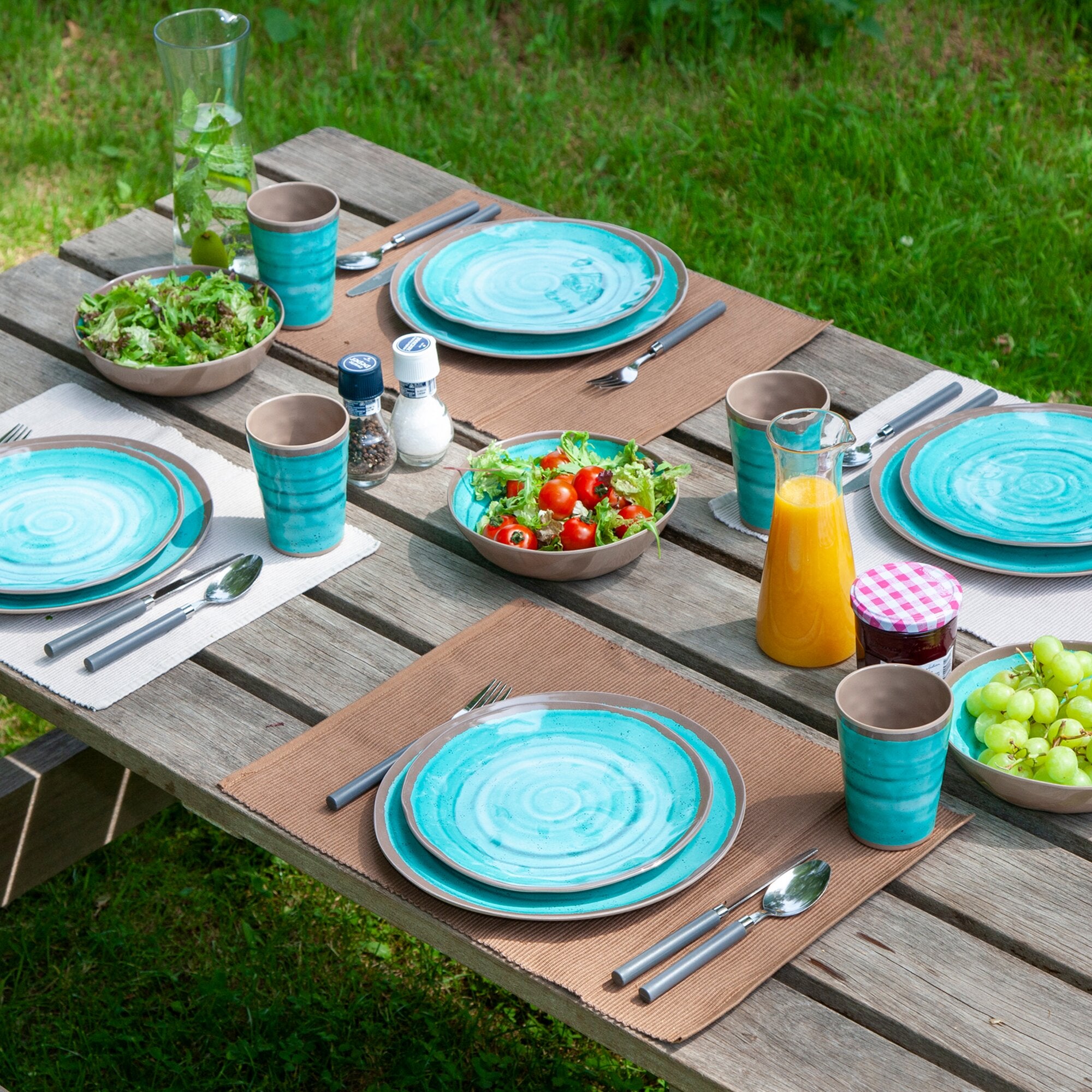 Außentisch mit Halo 12-teiligem aqua Geschirrset, türkisfarbene Teller, Schalen und Becher, Besteck, Salat, Tomaten und Orangensaft, Gras im Hintergrund
