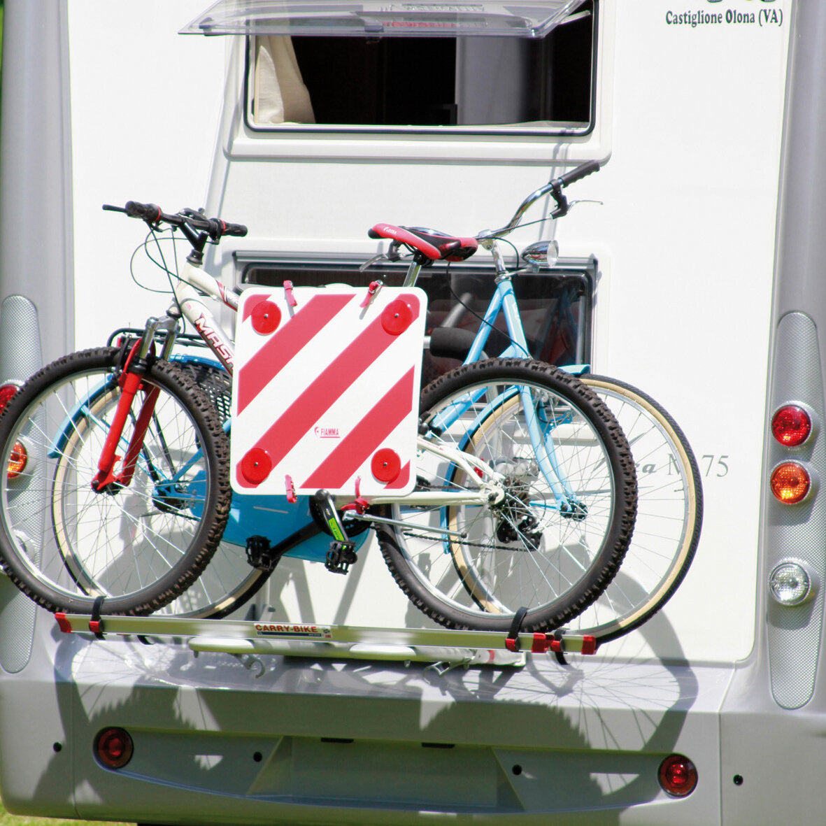 Rückseite eines weißen Fahrzeugs mit Fahrradträger Carry-Bike und zwei Fahrrädern davor eine diagonale rot-weiß gestreifte Warntafel mit roten Reflektoren