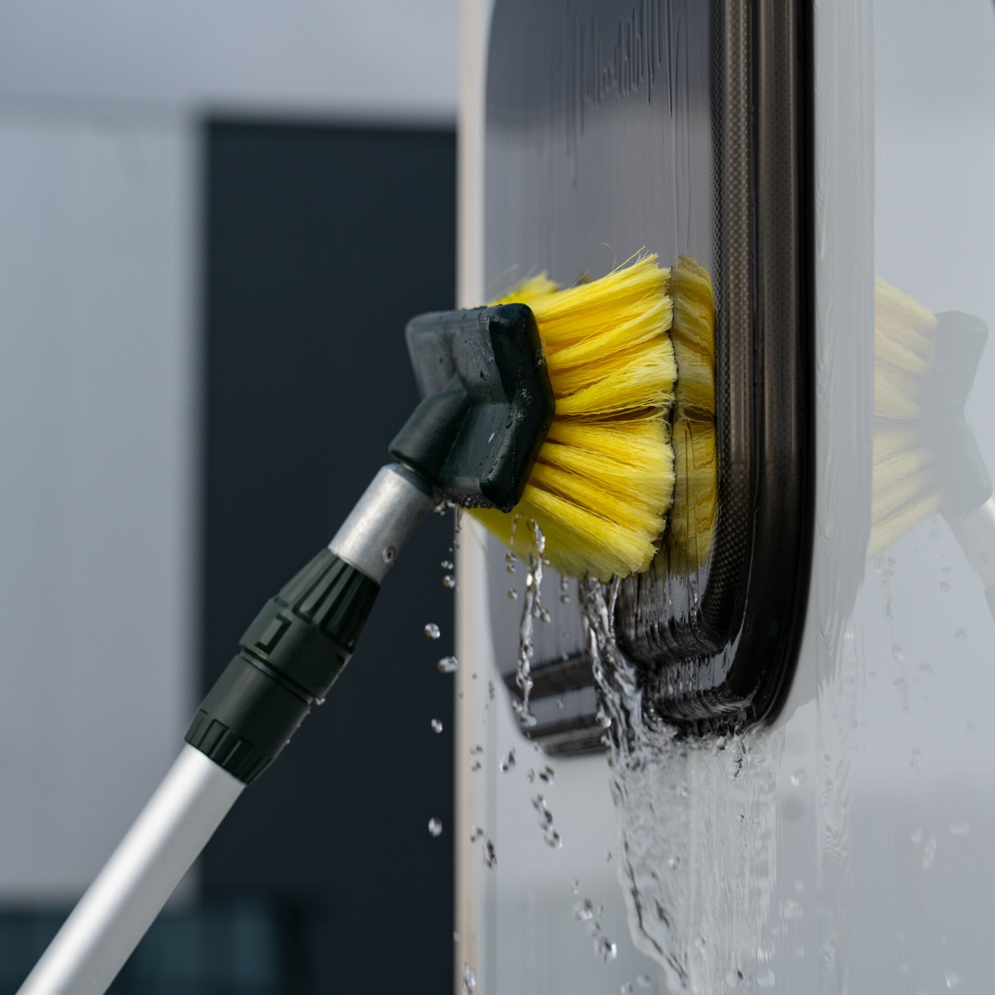 Waschbürste FF komplett, gelber Borstenkopf an einem Metallgriff, nah an einer glatten weißen Oberfläche, Wasser tröpfelt ab