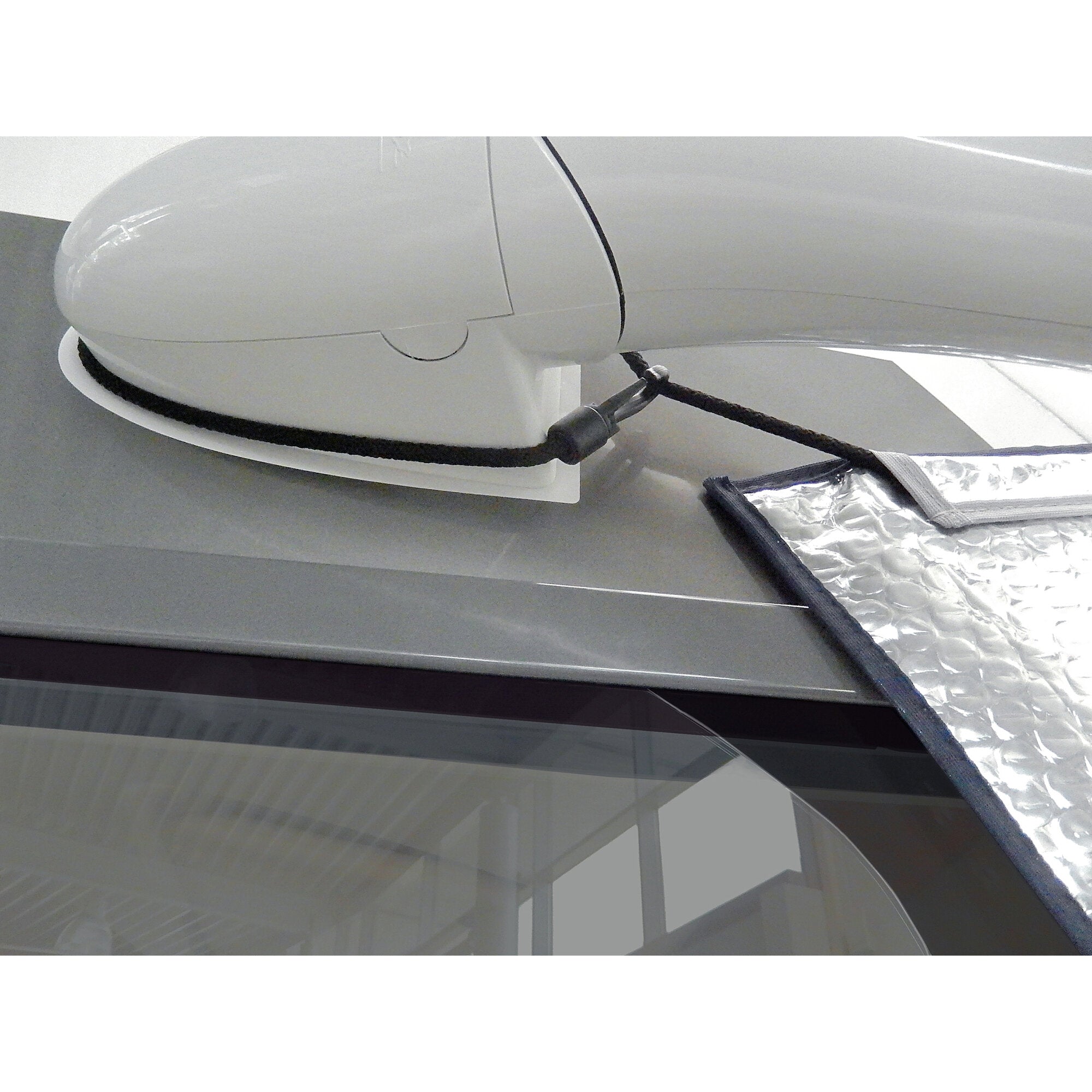 Weiße halbkugelförmige Gehäusekonstruktion mit vertikaler Trennlinie, schwarzes Kabel, daneben silberne Isolierfolie und Frontscheibe eines Autos