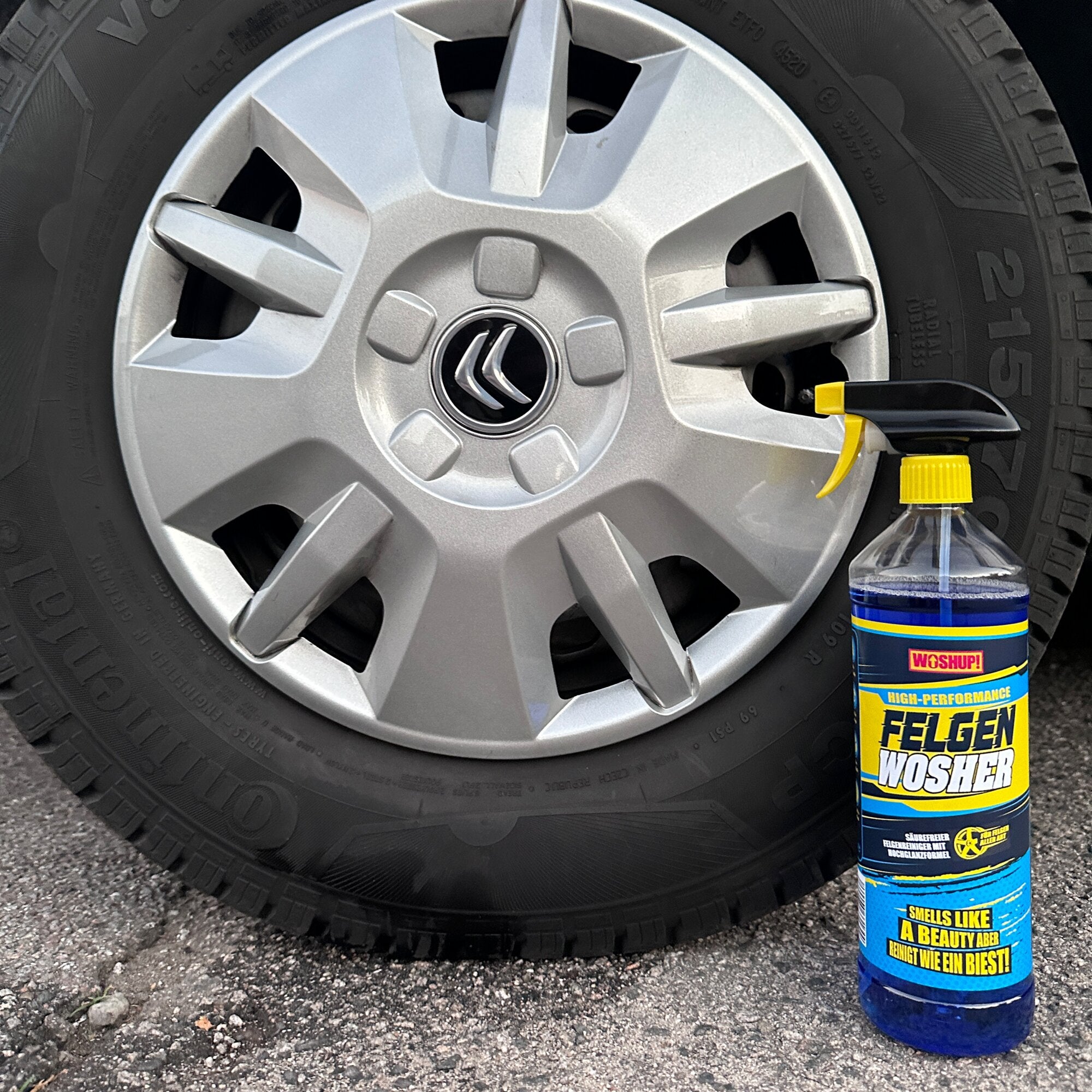 Nahaufnahme eines Autoreifens mit silberner Felge; rechts steht eine gelb-blau bedruckte 1-Liter-Flasche Felgenreiniger Wosher mit Sprühkopf