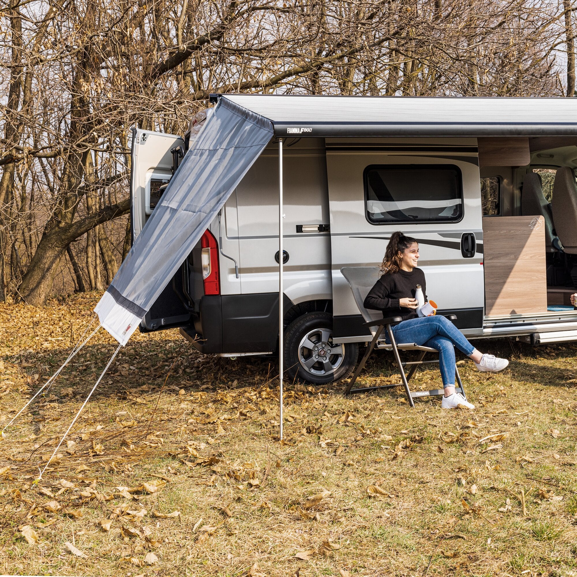 Seitenwand Sun View Side F45/F65/F80 am Wohnmobil mit ausziehbarem Seitenvorbau und grauer Abspannwand; Person sitzt in Klappstuhl mit Getränk