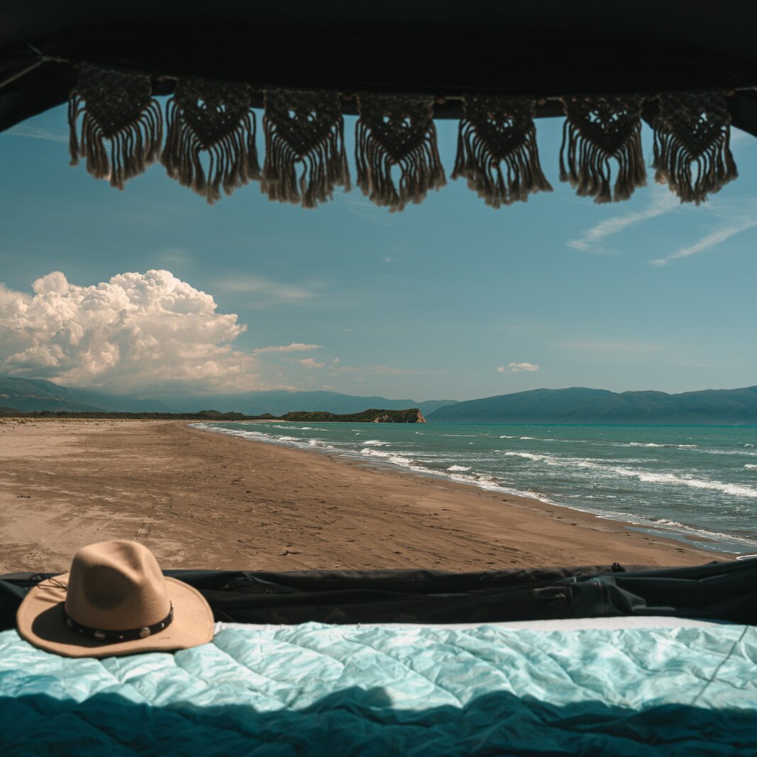 Innenansicht eines Dachzeltes Roof Space 4 mit blau gepolstertem Bett, braunem Hut und hängenden Fransen, Blick auf Strand, Meer und Berge