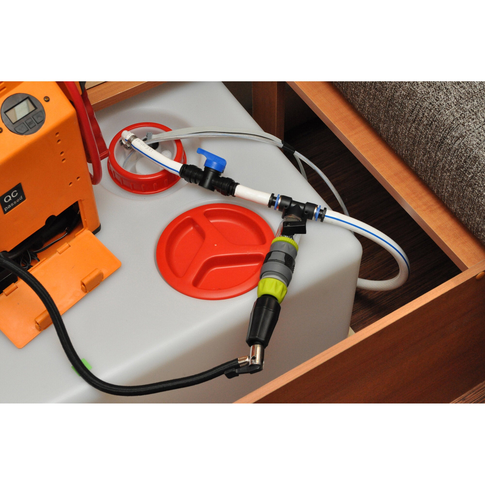 Orangefarbenes Steuergerät einer Entwässerungsausrüstung mit LCD-Anzeige, daneben Schläuche, ein weißer Tank mit roten Deckeln und Steckverbindungen