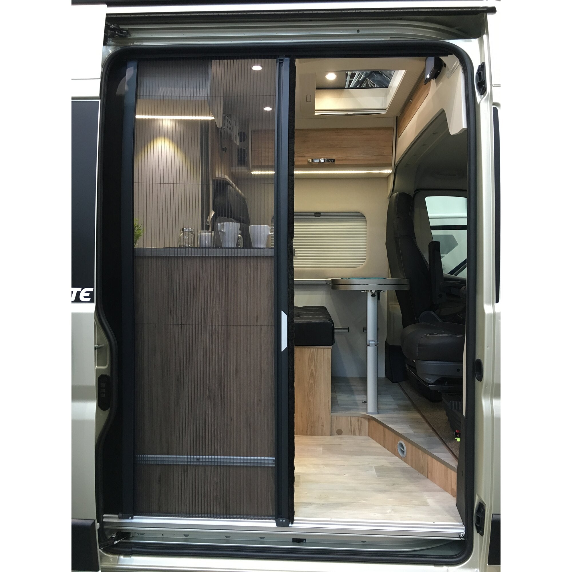 Innenansicht eines Campervans mit dunkler pleated Plissee-Fliegenschutztür in der Türöffnung, Holzmöbeln, LED-Beleuchtung und Fahrersitz im Hintergrund