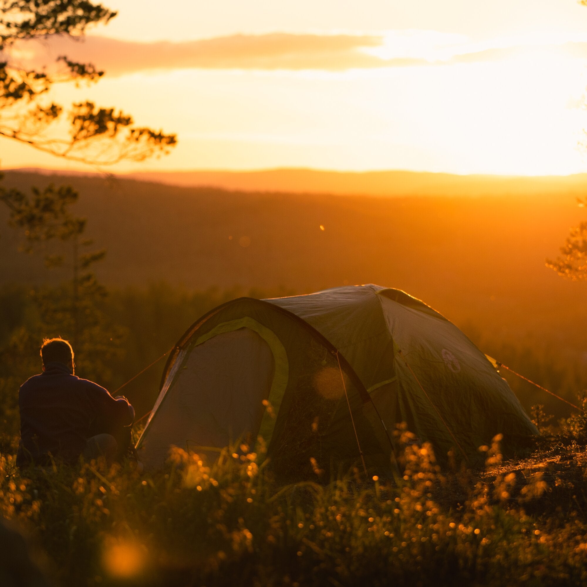 Abendliche Camping-Szene mit Kobuk Valley Plus Kuppelzelt im Vordergrund, grüne Hülle, rechts eine Person, goldenes Sonnenlicht
