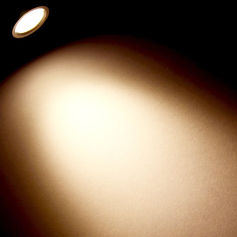 Kompakte Aufbauleuchte mit flexibel einstellbarem Schwanenhals und rundem LED-Lichtkopf; warmweißes Licht strahlt einen breiten Kegel auf eine Wand