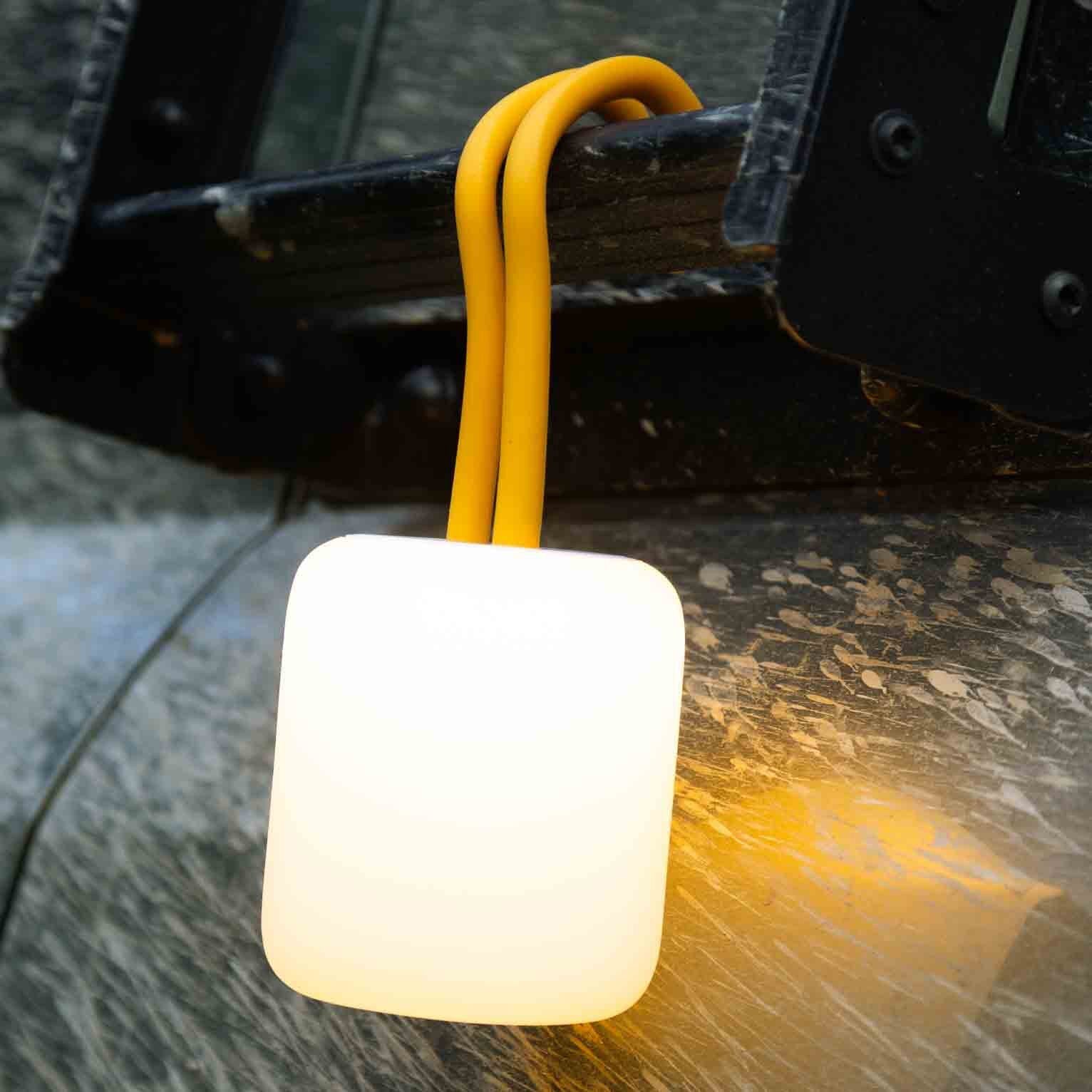 Orange Silikon-Schnüre der Campinglaterne Floppy um eine schwarze Metallhalterung geschlungen, darunter eine weiße Leuchte mit warmem Licht