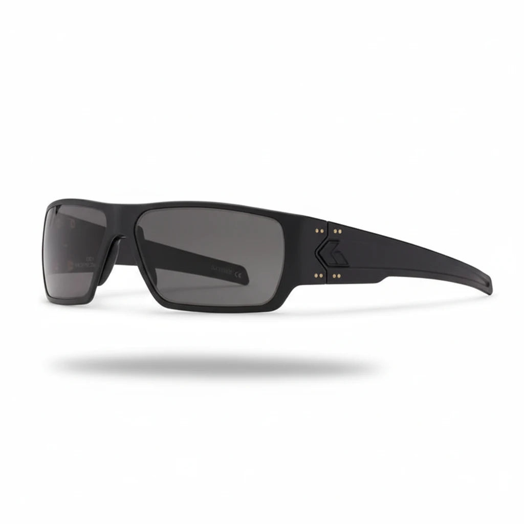 Schwarze robuste Schutzbrille mit rechteckigen, grauen Gläsern und markanten Seitenteilen mit goldfarbenen Schrauben,.