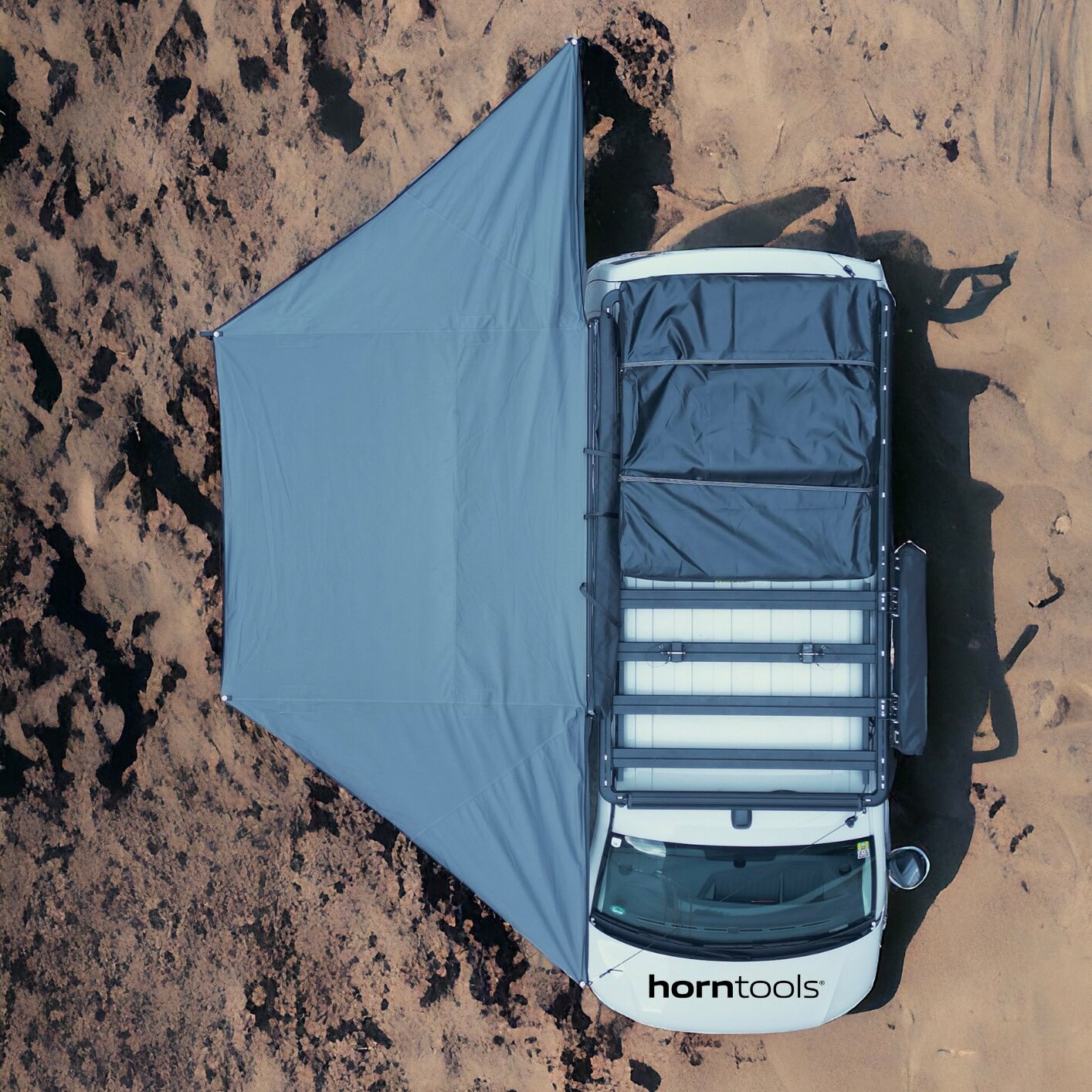 Draufsicht auf einen weißen Transporter mit einer großen blauen Horizon Markise 180°, 200 cm, seitlich ausgeklappt vor sandigem Untergrund