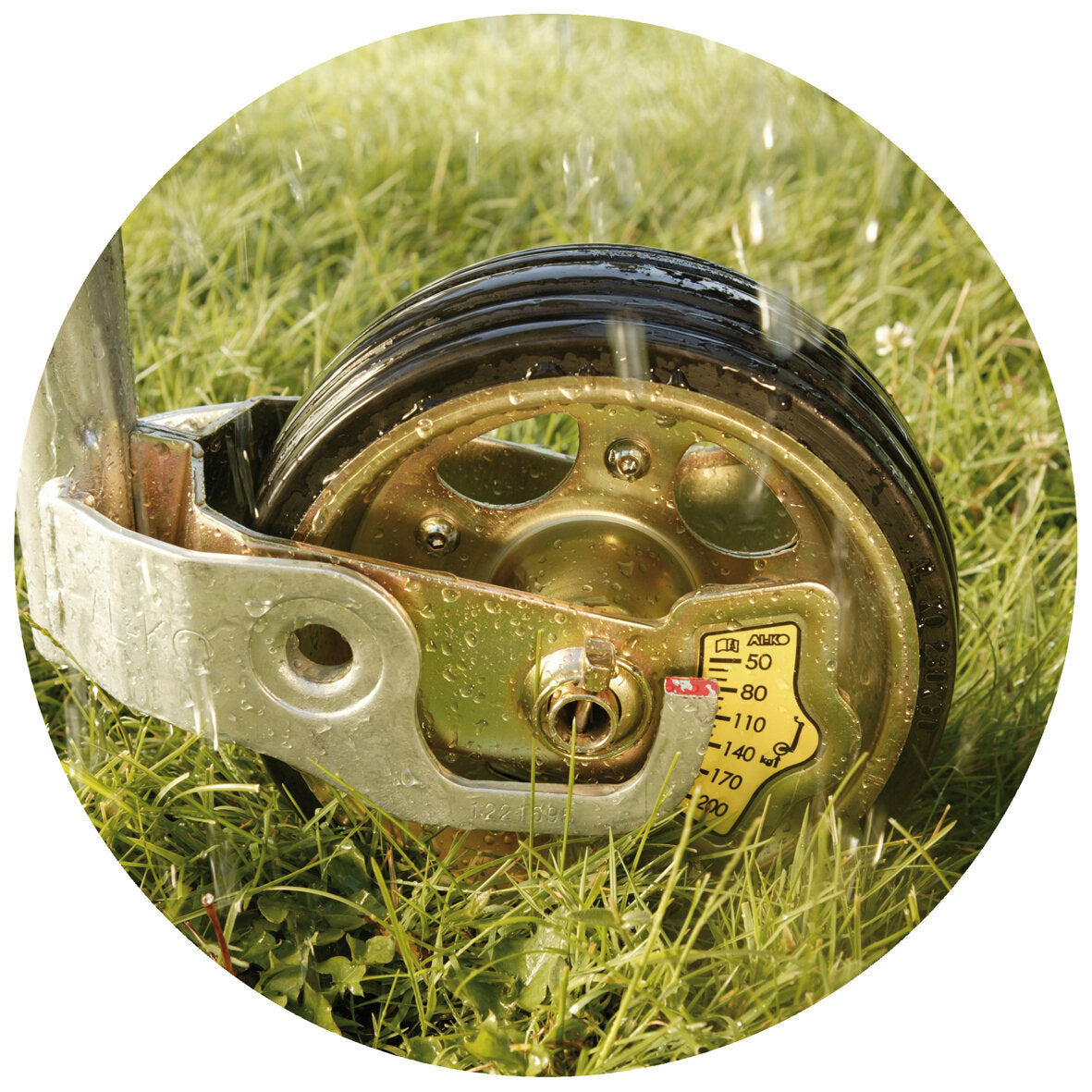Stützrad Premium: Nahaufnahme eines Metallrahmens mit Rad, goldene Felge, schwarzer Reifen, Gras im Hintergrund, Tau, gelbes Kennzeichen