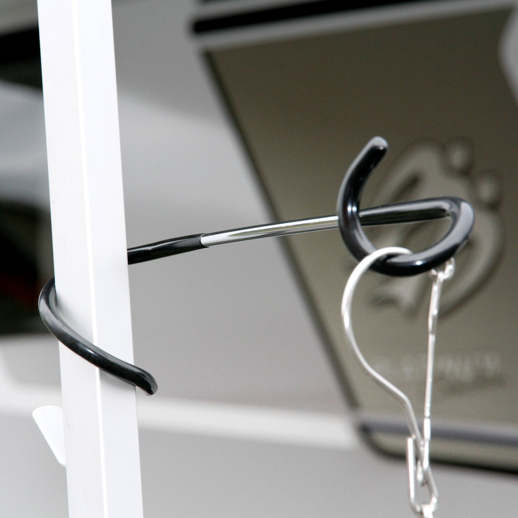 Nahaufnahme eines weißen Regalrahmens mit einem schwarzen Unifix Universalhaken an einer Metallstange, daneben liegen lose Kabel