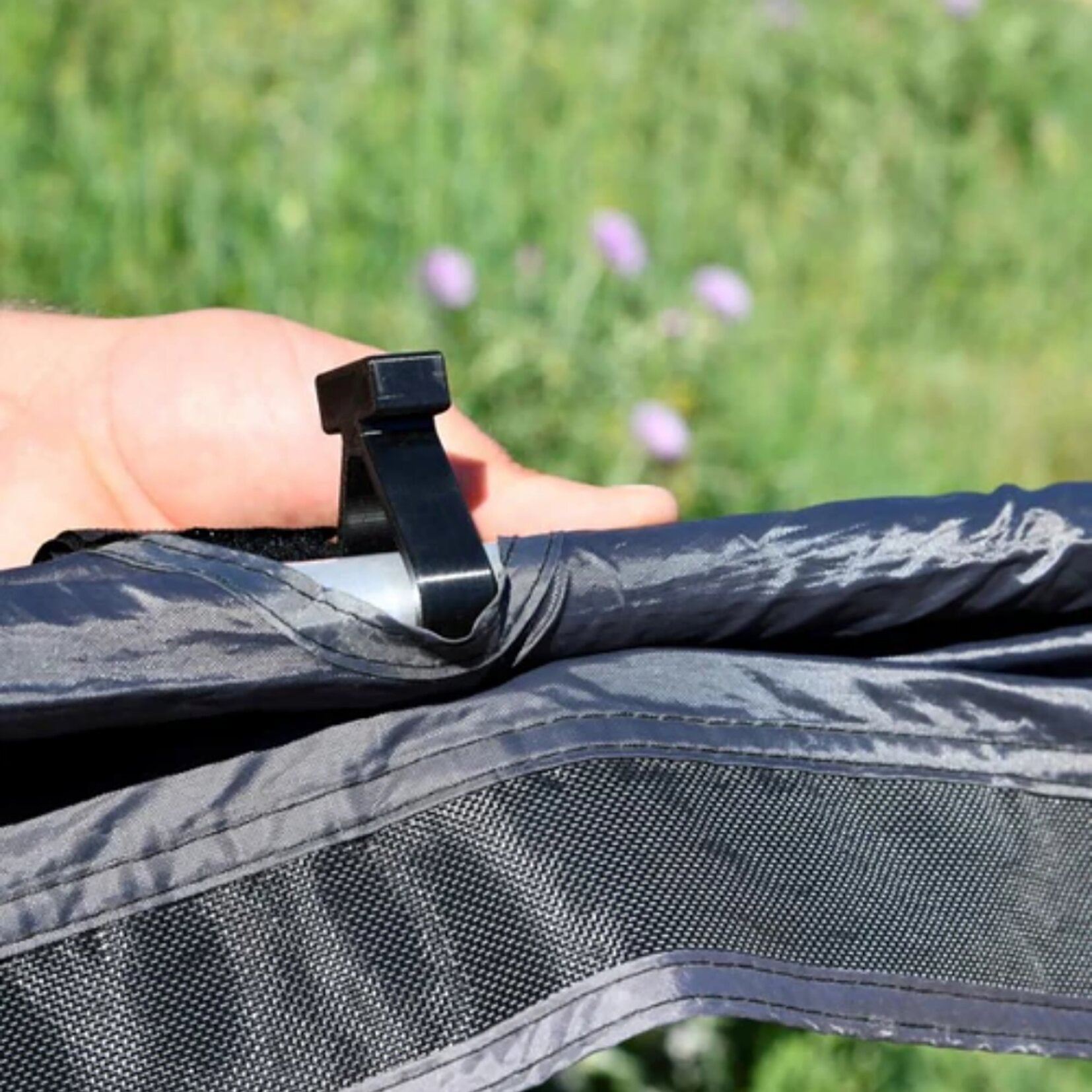 Nahaufnahme eines schwarzen Kunststoff-Adapters für C-Schienen, befestigt an einer grauen Stoffoberfläche mit Nähten, unscharfer grüner Hintergrund
