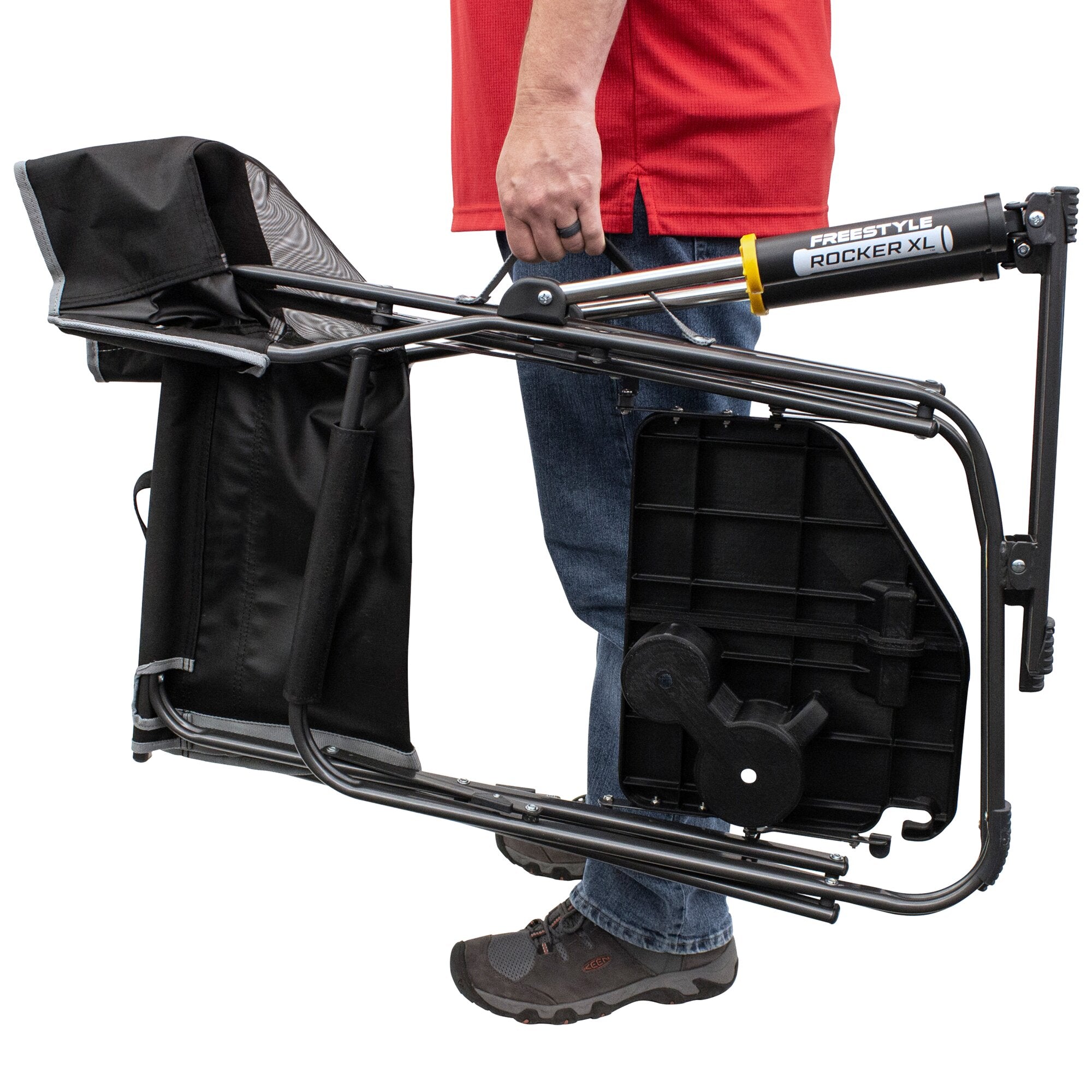 Person in rotem Oberteil hält Camping-Schaukelstuhl Freestyle Rocker XL zusammengefaltet; schwarze Stoffbespannung, Metallrahmen und gelber Verriegelungsring