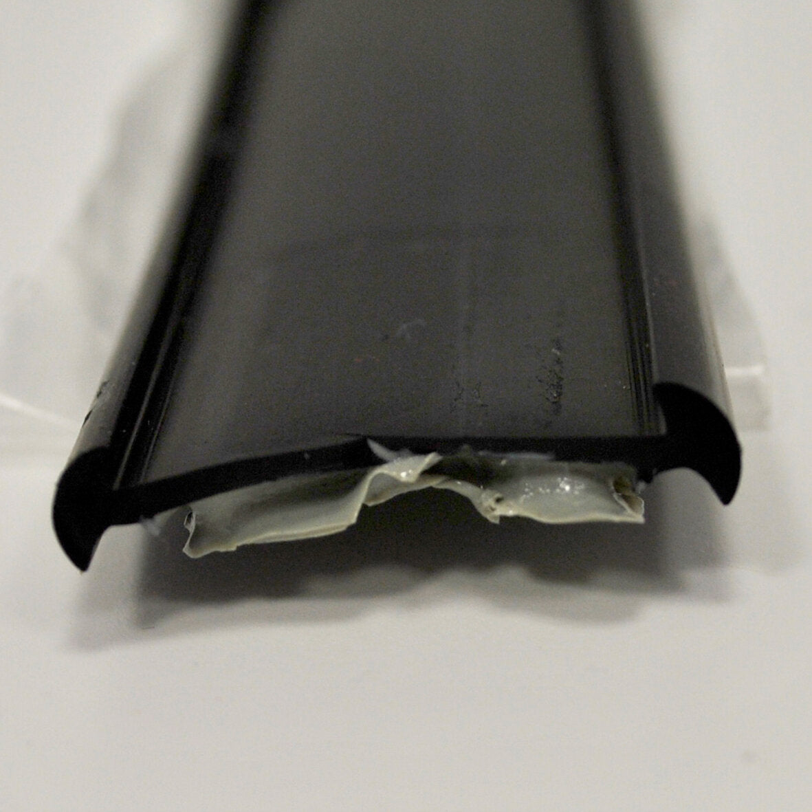 Schwarze Gummiunterlage in U‑Profilform, flache Oberseite und seitlich nach außen gebogene Enden, Kleberreste an der Unterkante