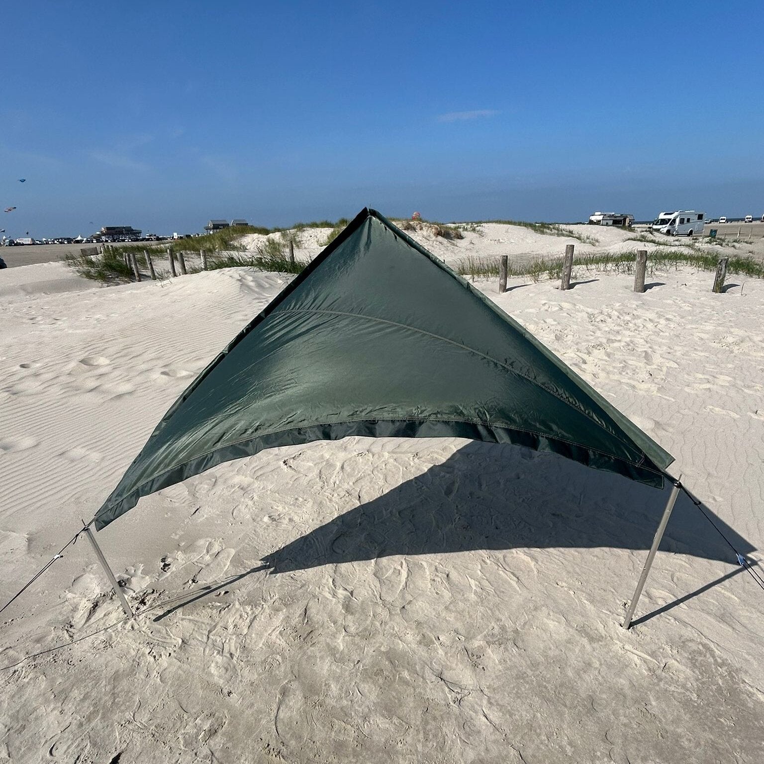 Grünes Sonnensegel Zip Protect Canvas Single in Jungle, dreieckig auf Sand gespannt mit Abspannleinen; Dünen und Autos im Hintergrund