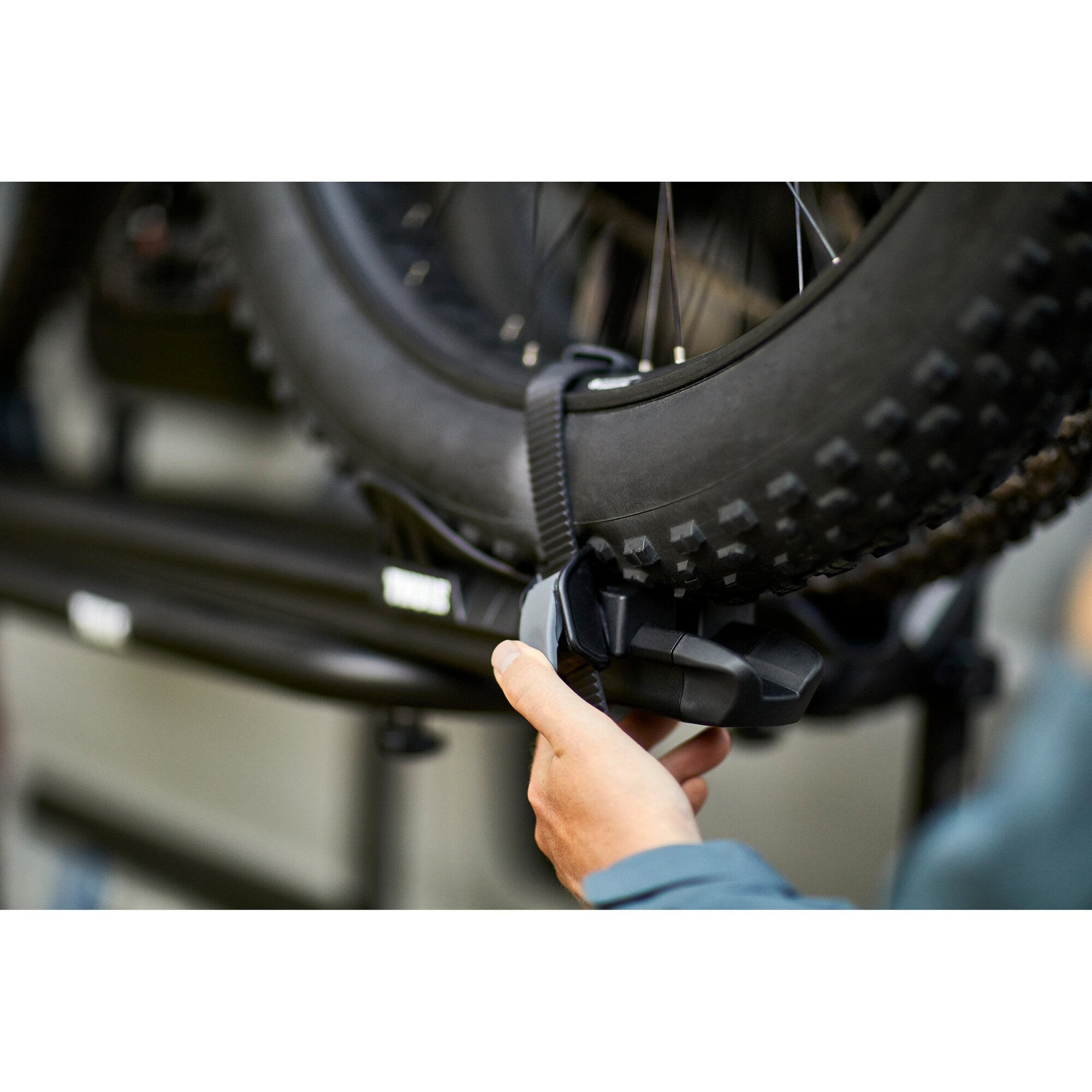 Detailaufnahme einer Hand, die eine schwarze Halterung an einem Fatbike-Träger befestigt, neben einem grob profilierten Reifen mit Stollen