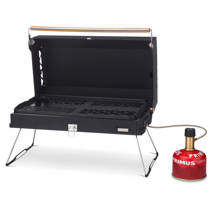 Schwarzer Kuchoma Gasgrill mit geöffnetem Deckel, Metallrost, klappbare Drahtbeine, rechts rote Gasflasche mit Schlauchanschluss