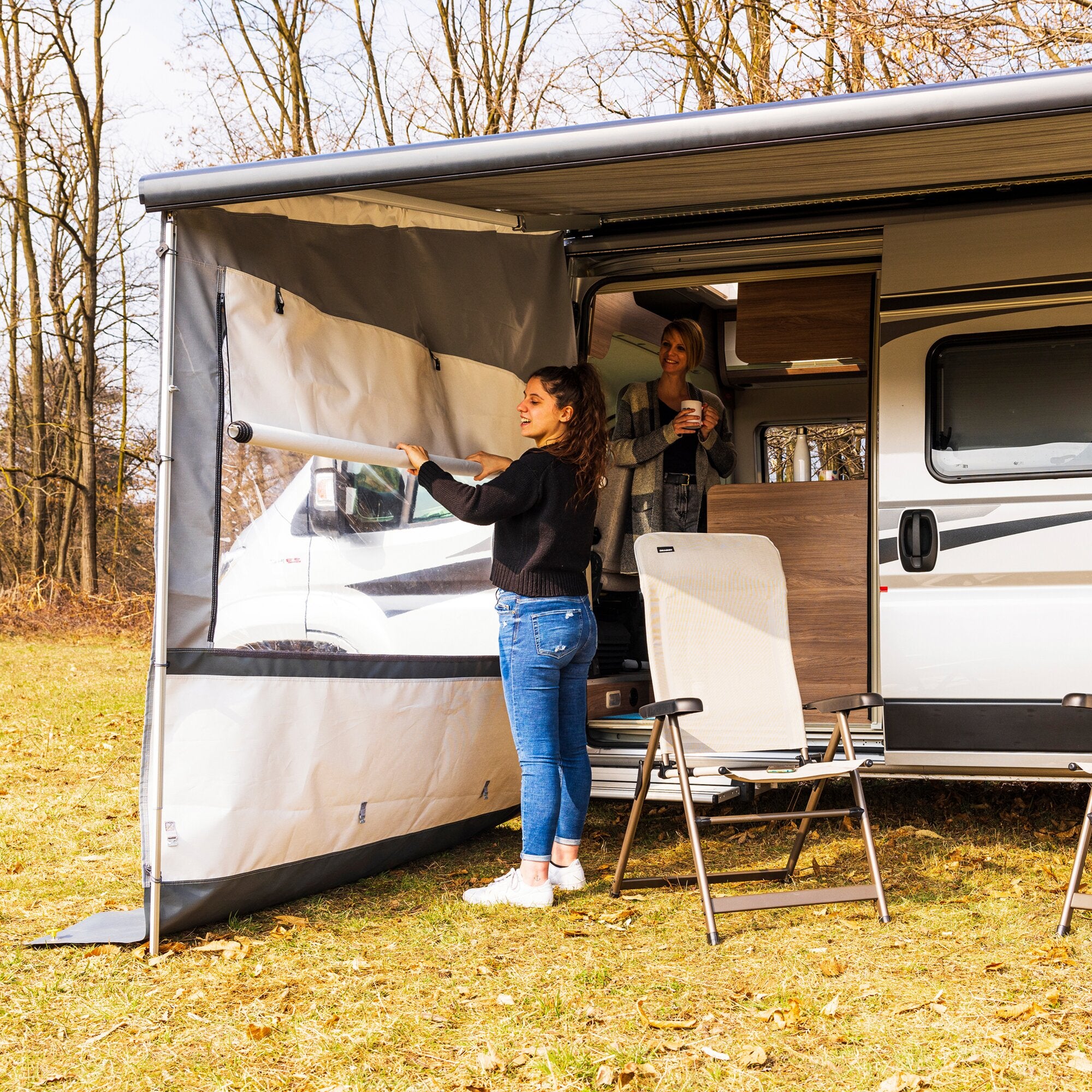Linke Seitenwand eines Wohnmobils mit offener Stoffwand; Innenraum sichtbar, zwei Frauen stehen im Wagen, eine hält einen Becher