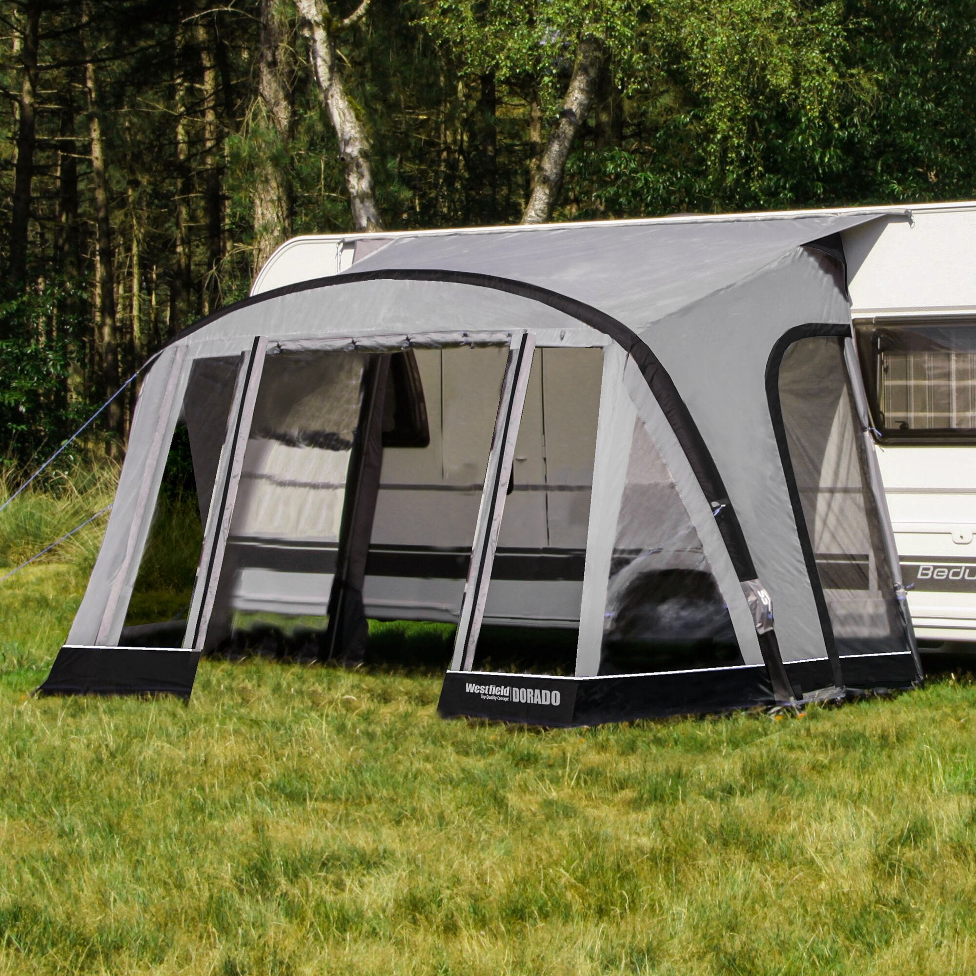 Teilzelt Dorado XL in Grau mit großen Fensterflächen und Rundbogenfront, am Wohnwagen angebaut, Gras und Wald im Hintergrund