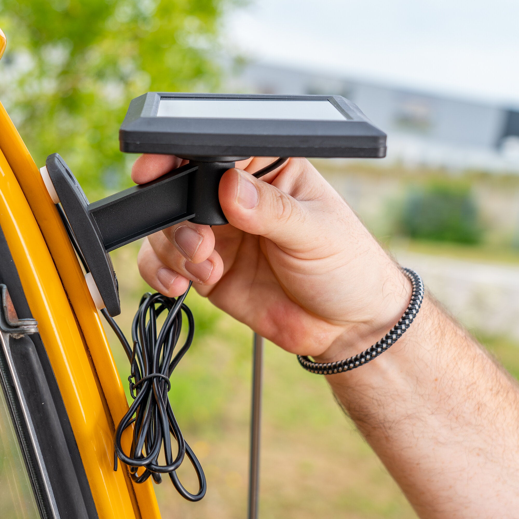 Hand hält ein schwarzes flaches Display-Modul mit Halterung an einem gelben Rahmen; mehrere Kabel hängen lose herab