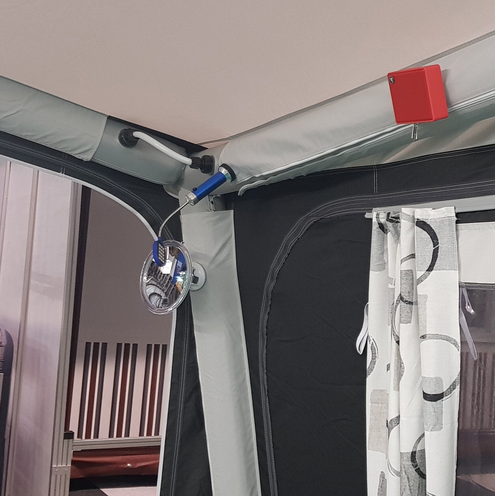 Innenraum eines Campingzelts mit Stoffwänden, rotem Rechteckmagnet am Metallrahmen, blauem Zylindermagnet und rundem Spiegel an Schnur, gemusterte Vorhänge