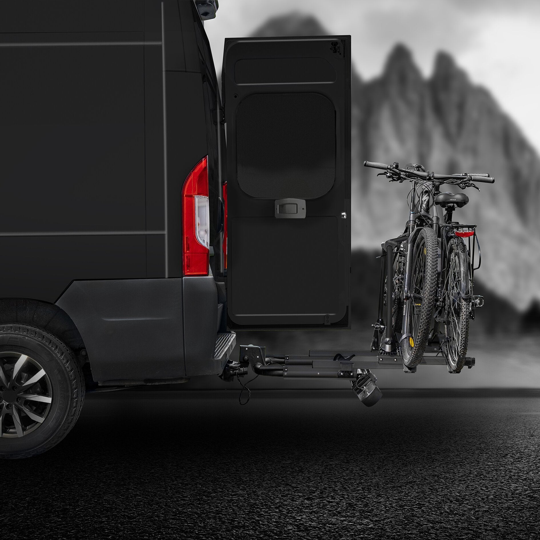 Schwarzer Fahrradträger SD260 an der Anhängerkupplung eines Transporters, zwei Fahrräder darauf montiert, Berglandschaft unscharf