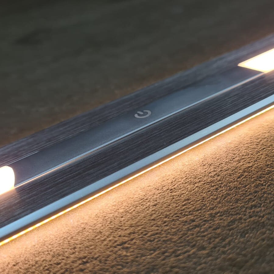 Detailaufnahme einer silbernen Metallleiste mit Power-Symbol und integrierter warmer Ambientebeleuchtung entlang der unteren Kante