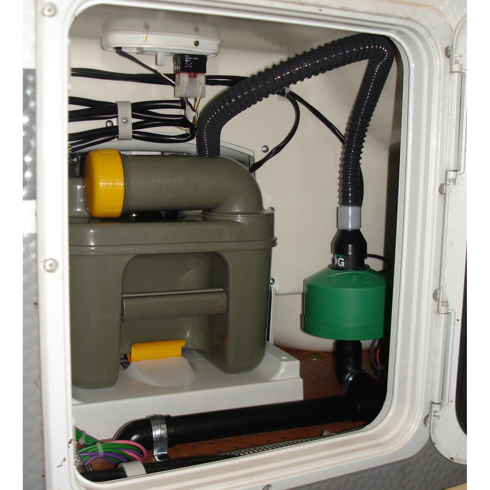 Innenansicht eines weißen Türschranks mit elektrischer WC-Entlüftung C200; sichtbare Kabelbündel, Schläuche, olivegrüner Tank mit gelbem Deckel