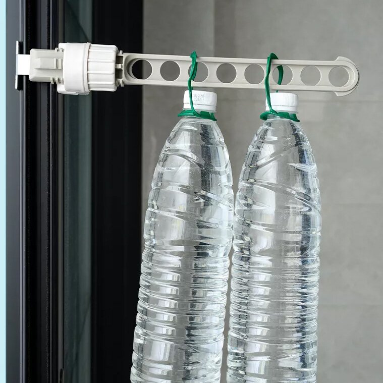 Klemm-Wäschetrockner aus hellem Kunststoff an Fensterrahmen befestigt, Querträger mit Löchern hält zwei Plastikflaschen an grünen Kabelbindern