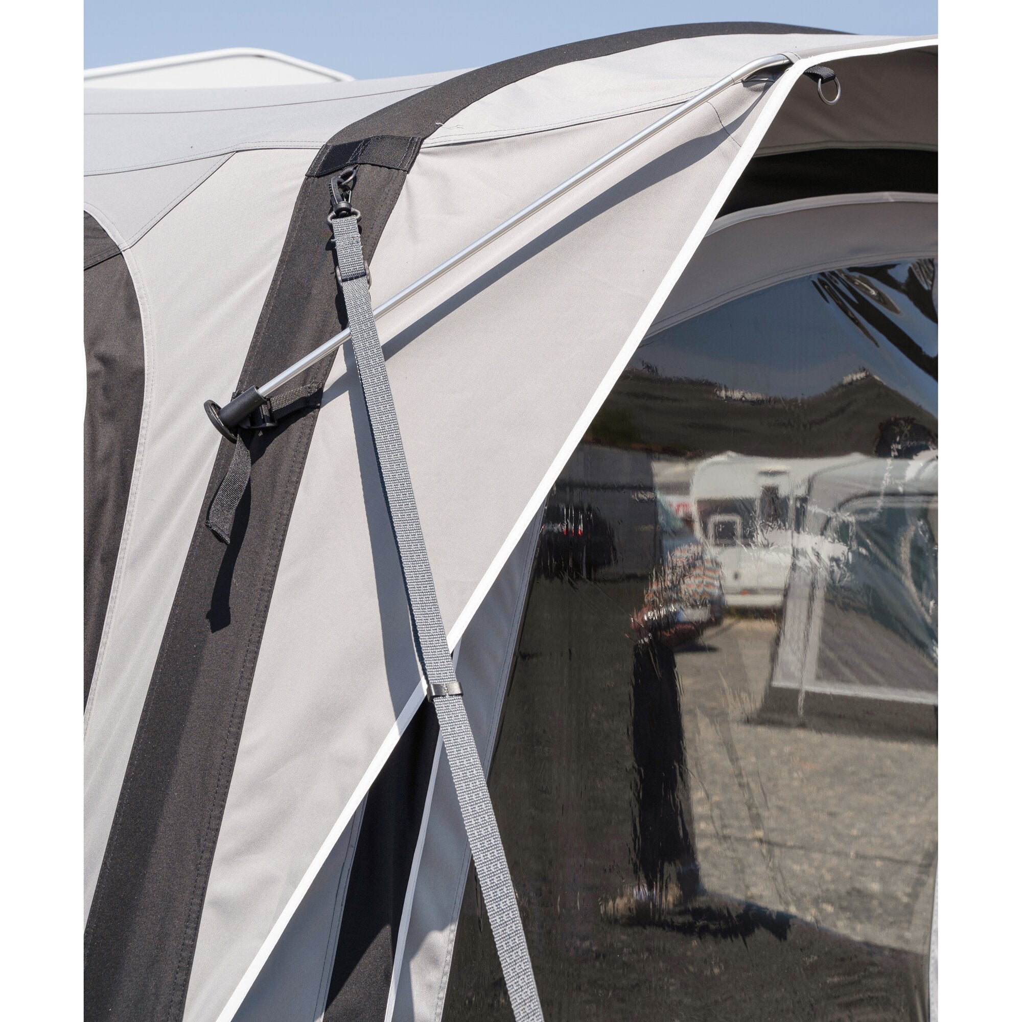 Detailaufnahme eines Reisemobilvorzelts: graue Stoffbahn mit dunklem Streifen, silberne Stange, Gurtband mit Schnalle, transparentes Fenster mit Reflexion