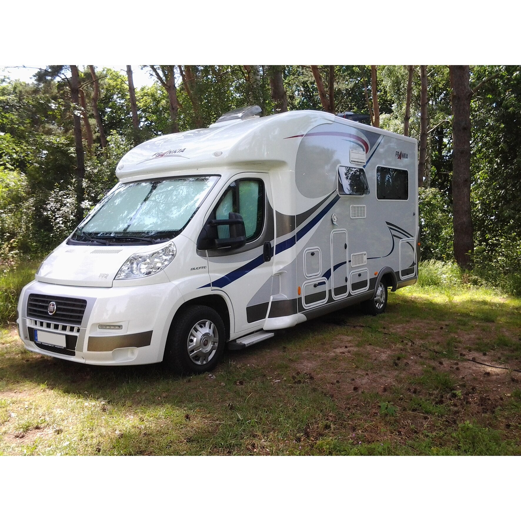 Weißer Fiat Ducato basierter Wohnmobil-Camper mit farbigen Dekorstreifen, Fenstern und Dachklimaanlage steht in einem Waldgebiet