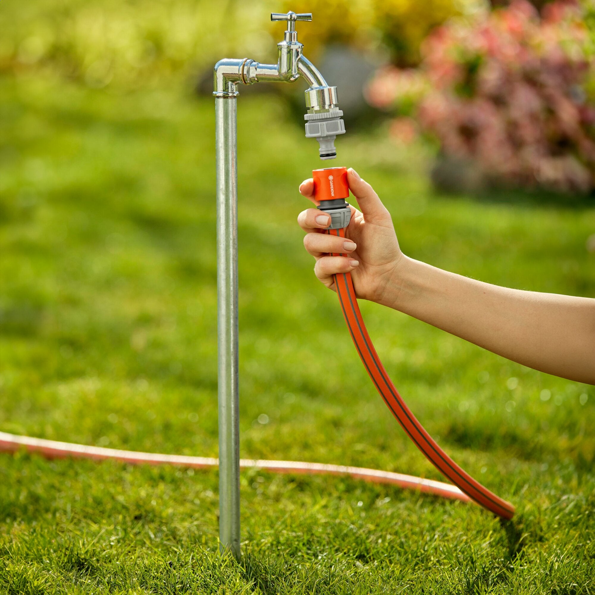 Hahnverbinder aus Metall am Wasserhahn, ¾ Zoll, mit grauem Schnellverbinder; orange Schlauchkupplung wird von einer Hand gehalten