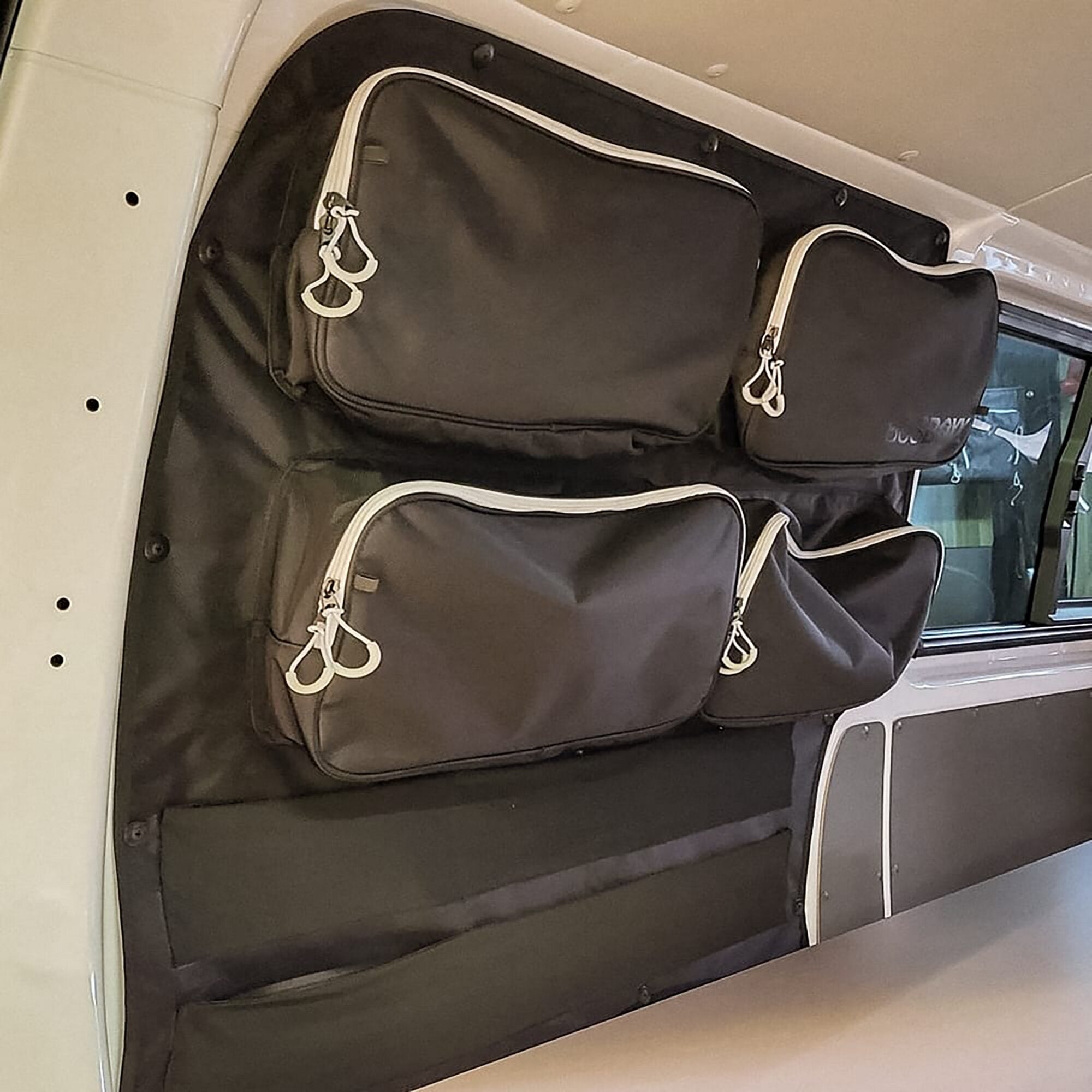 Schwarze Organizer-Tasche aus Stoff mit weißen Reißverschlüssen, an der Fahrerseite des Innenraums befestigt, mehrere Taschen sichtbar