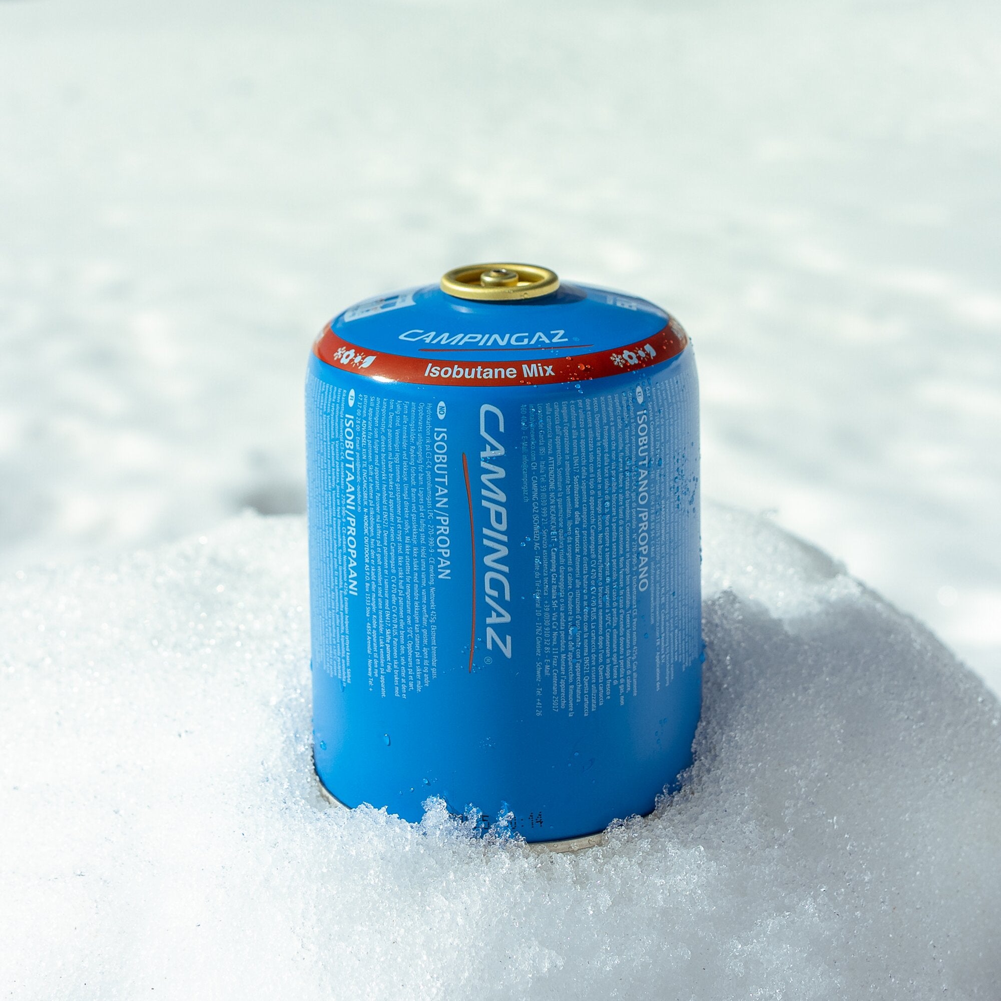 Nahaufnahme einer blauen Gaskartusche mit goldener Ventilabdeckung auf schneebedecktem Untergrund; vorne lesbar CAMPINGAZ Isobutane Mix