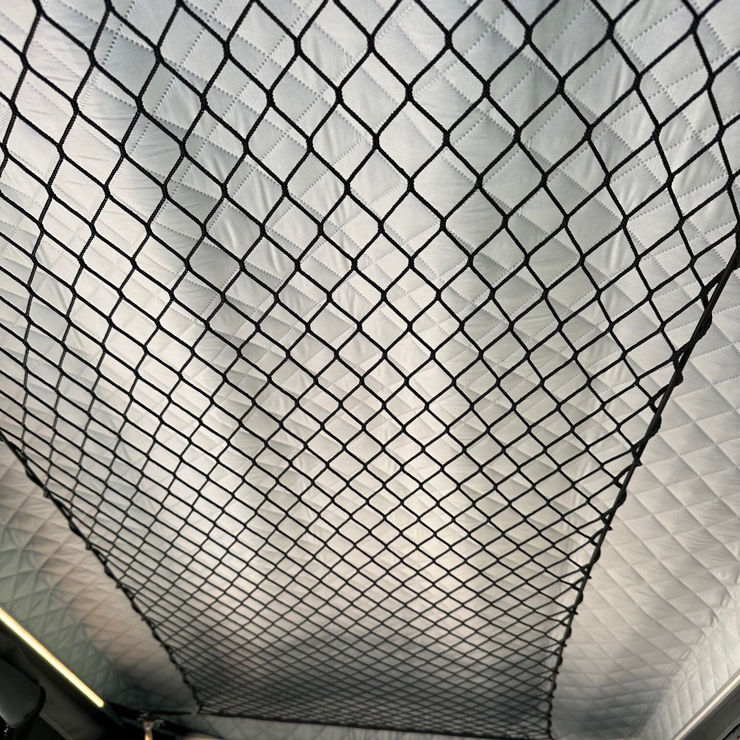 Innenraum eines Dachzelts Zambezi mit dem schwarzen diagonalen Gitternetz als Aufbewahrungsgitter vor einer quiltartigen Innenverkleidung