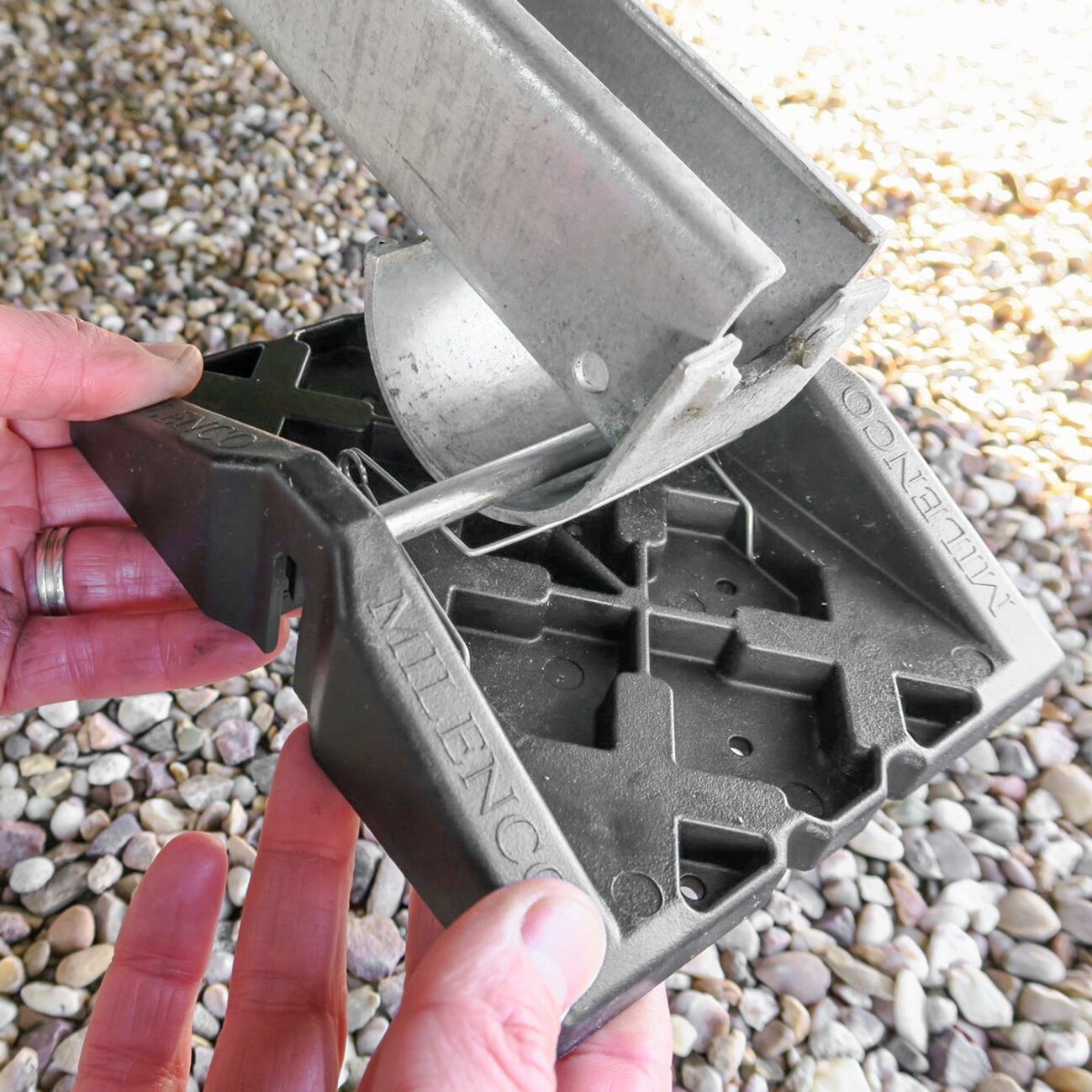 Hand hält ein Stützplattenset Corner Feet, schwarze Kunststoffbasis mit Metallhalterung, Metallstange wird eingeführt, Kiesboden im Hintergrund