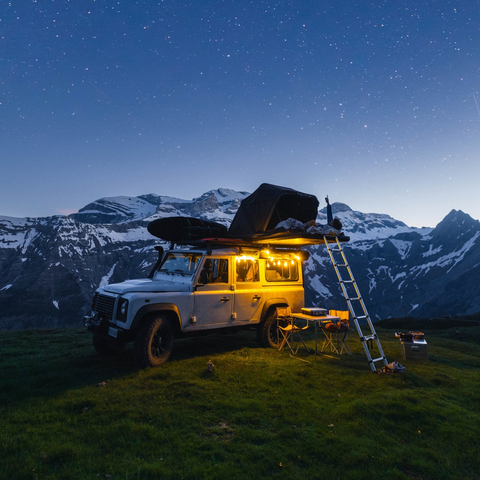 Dachzelt Roof Space 2 auf weißem Geländewagen mit Leiter, Campingstühle und Tisch, Berglandschaft mit Schnee und Sternenhimmel